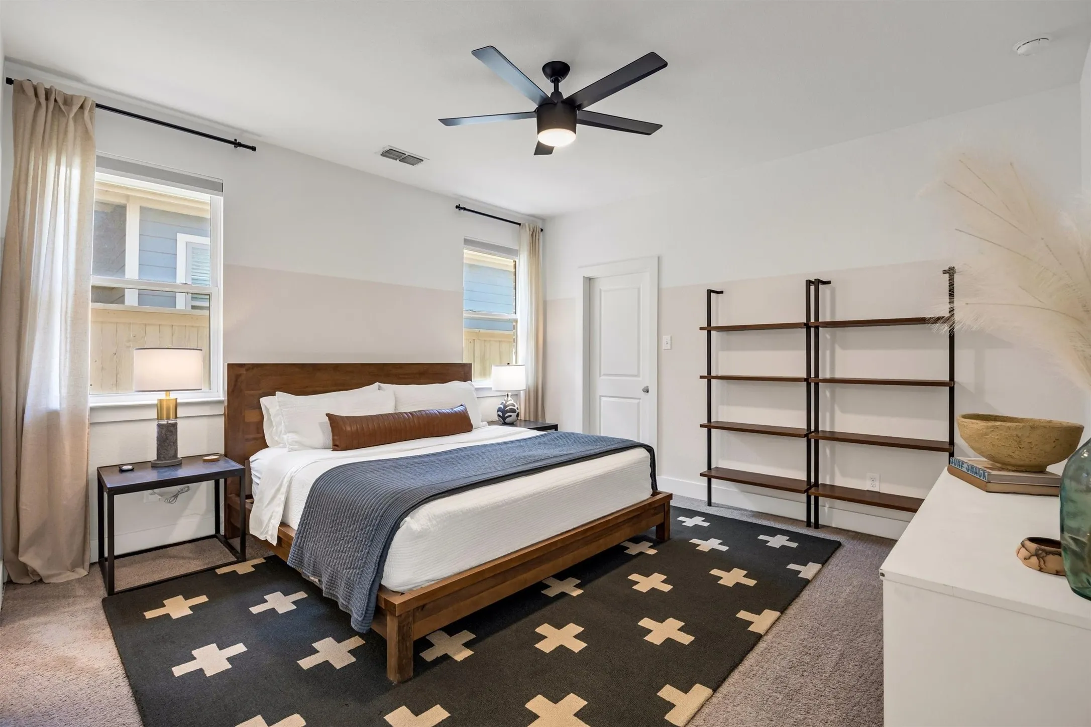 Wall-mounted shelving unit, ceiling fan with integrated lighting, wood-finish headboard, and dual windows