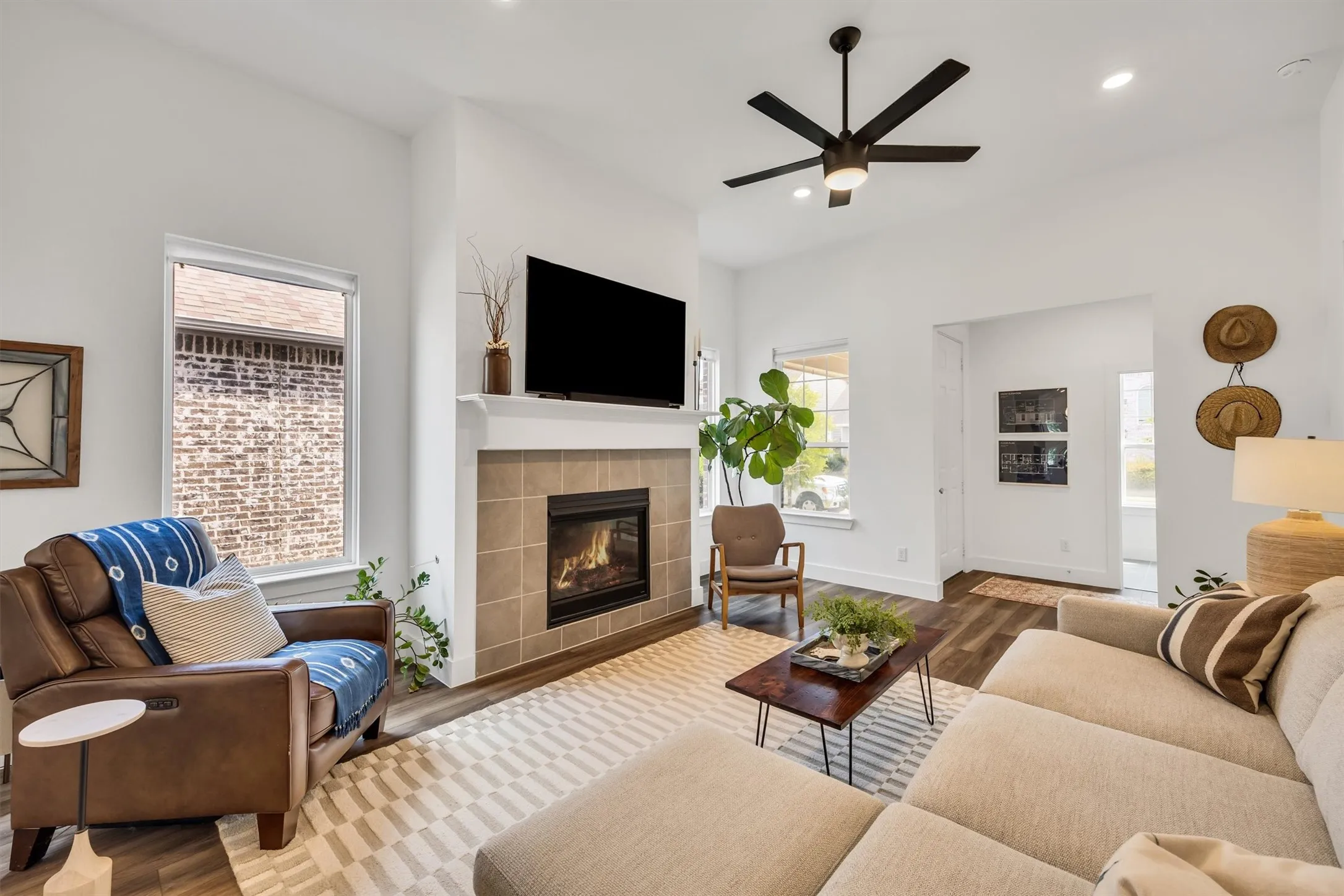 Integrated fireplace with tile surround, wood-finish flooring, ceiling fan with integrated lighting, recessed lighting, and white trim