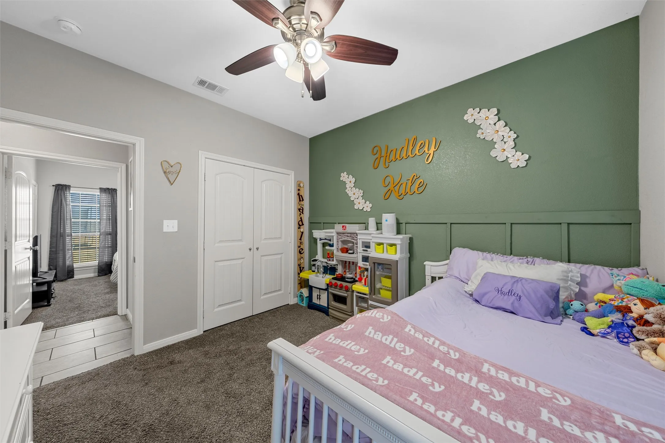 Ceiling fan with light kit, gray carpeting, dual-door closet, green accent wall, and decorative paneling