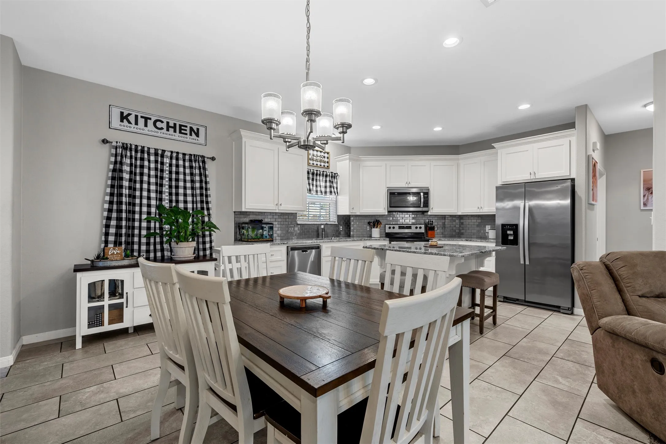 Open-concept kitchen featuring white cabinetry, stainless steel appliances, a center island with bar seating, and tile flooring