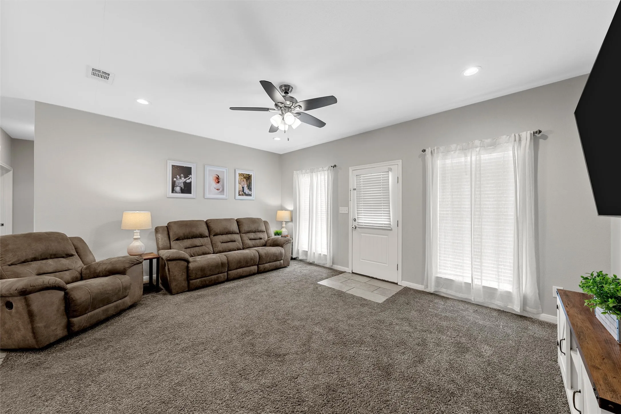 Spacious living area featuring neutral carpeting, a ceiling fan, recessed lighting, and two large windows with blinds