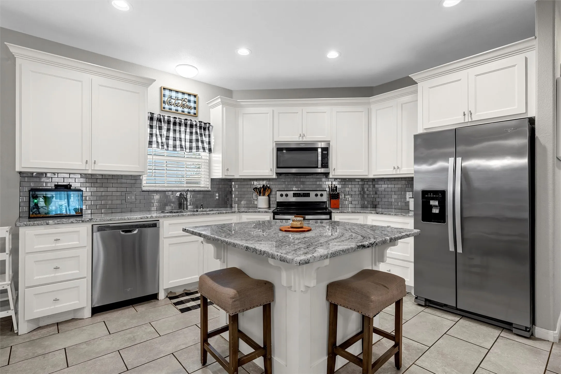 White cabinetry, stainless steel appliances, subway tile backsplash, granite countertops, and recessed lighting