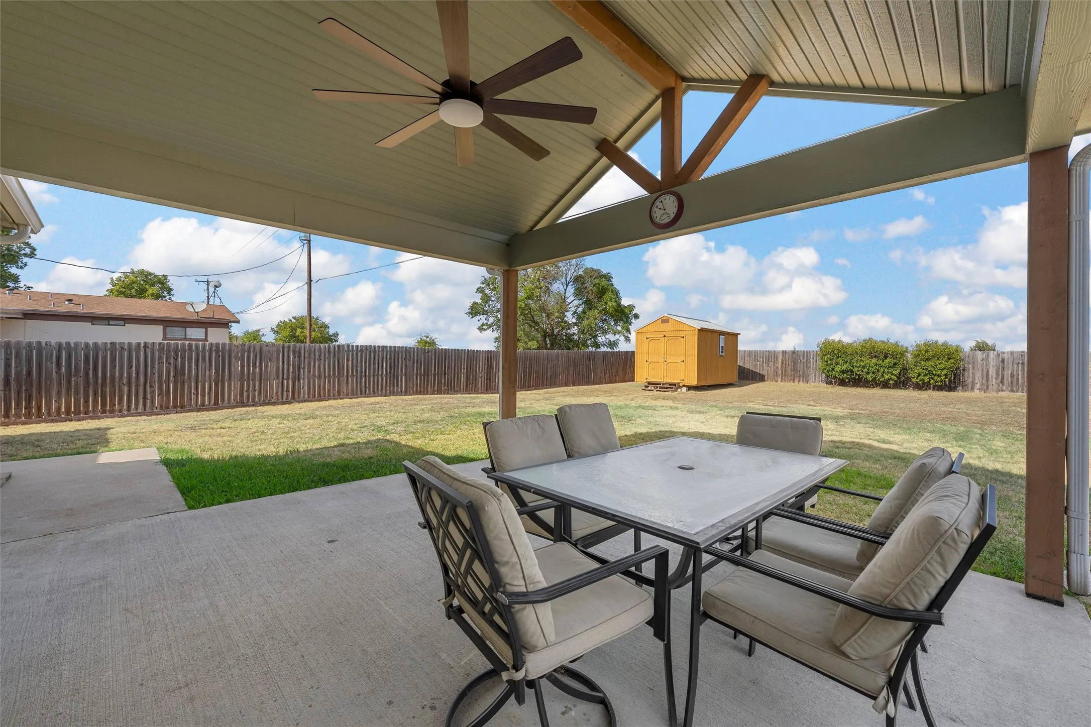 Covered patio with a ceiling fan, concrete flooring, and a shed in the background