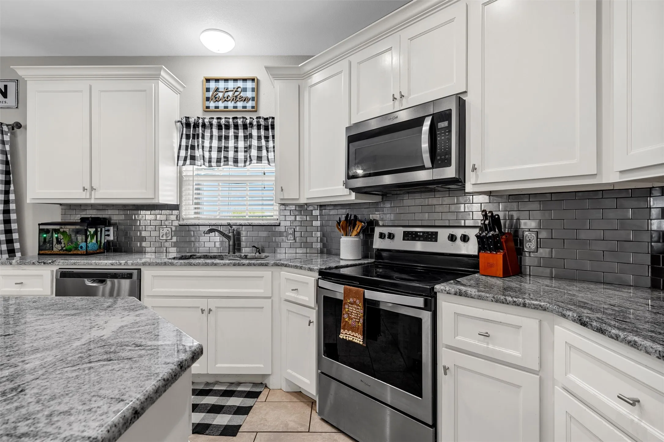 White cabinetry, stone countertops, subway tile backsplash, stainless steel appliances, and tile flooring