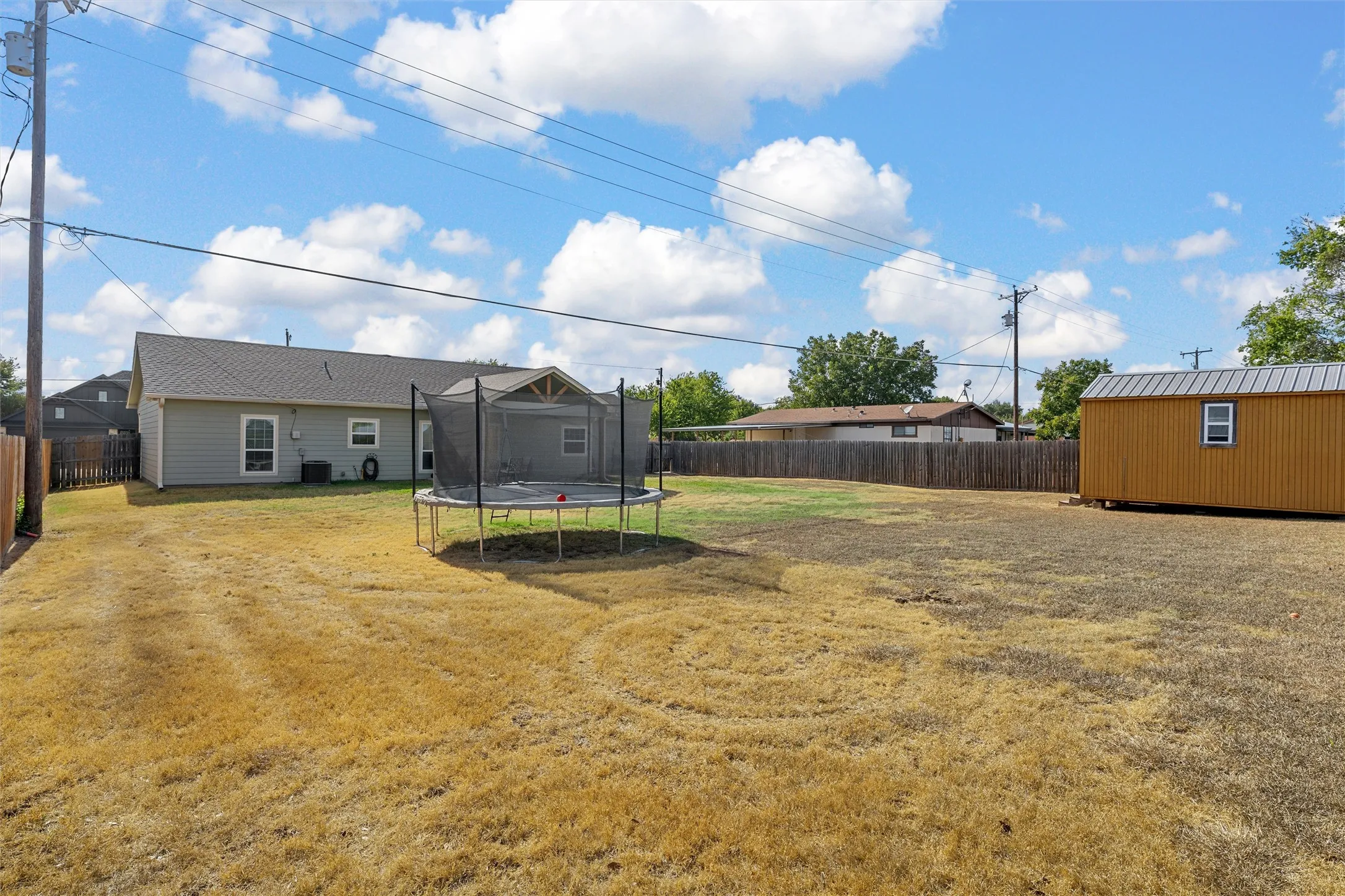 Expansive backyard featuring a fenced perimeter, a detached auxiliary building with a metal roof, and a single-story residence with a pitched roof