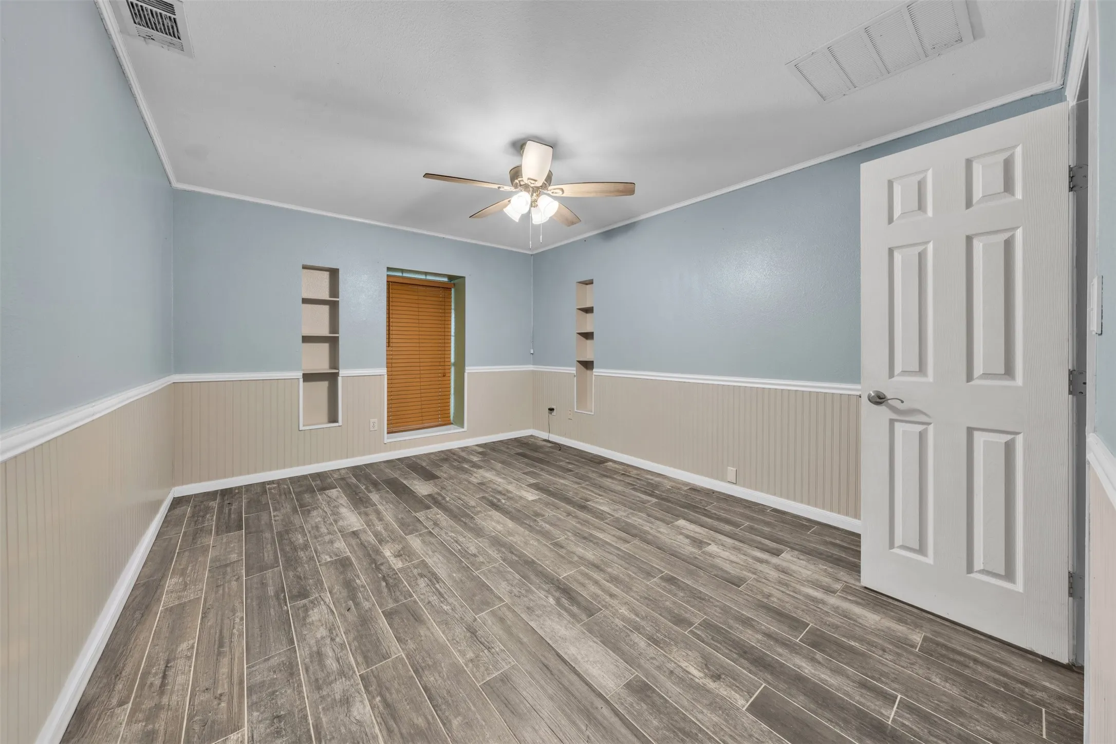 Wood-finish flooring, two-tone wall treatment, built-in wall shelving, and a ceiling fan with integrated lighting