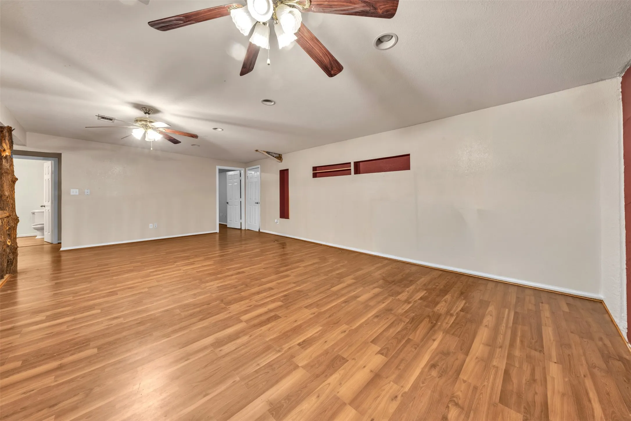 Spacious room with wood-finish flooring, multiple ceiling fans, recessed lighting, and built-in wall alcoves