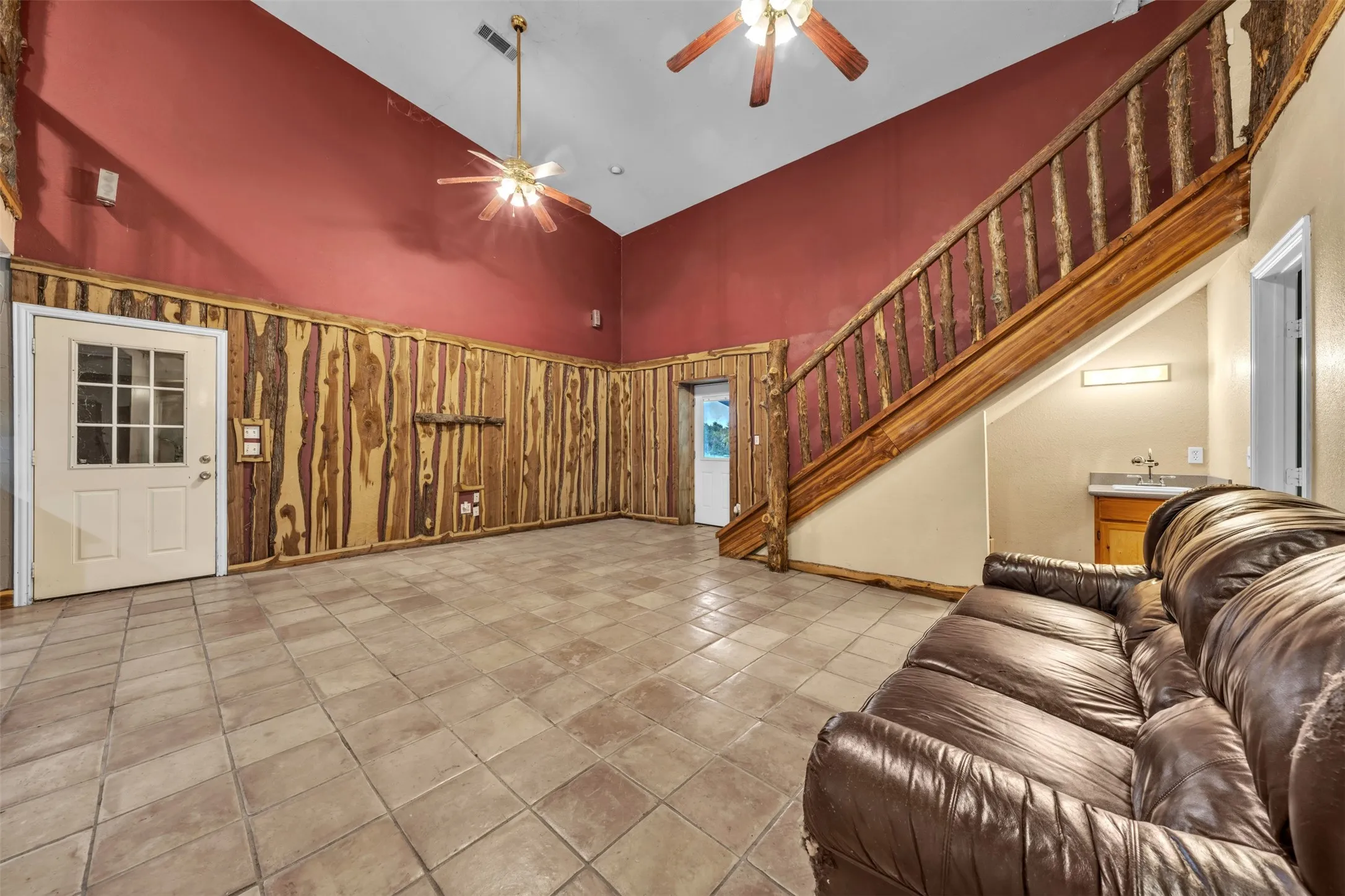 Vaulted ceiling with dual ceiling fans, tile flooring, natural wood paneling, and a natural wood staircase with railing