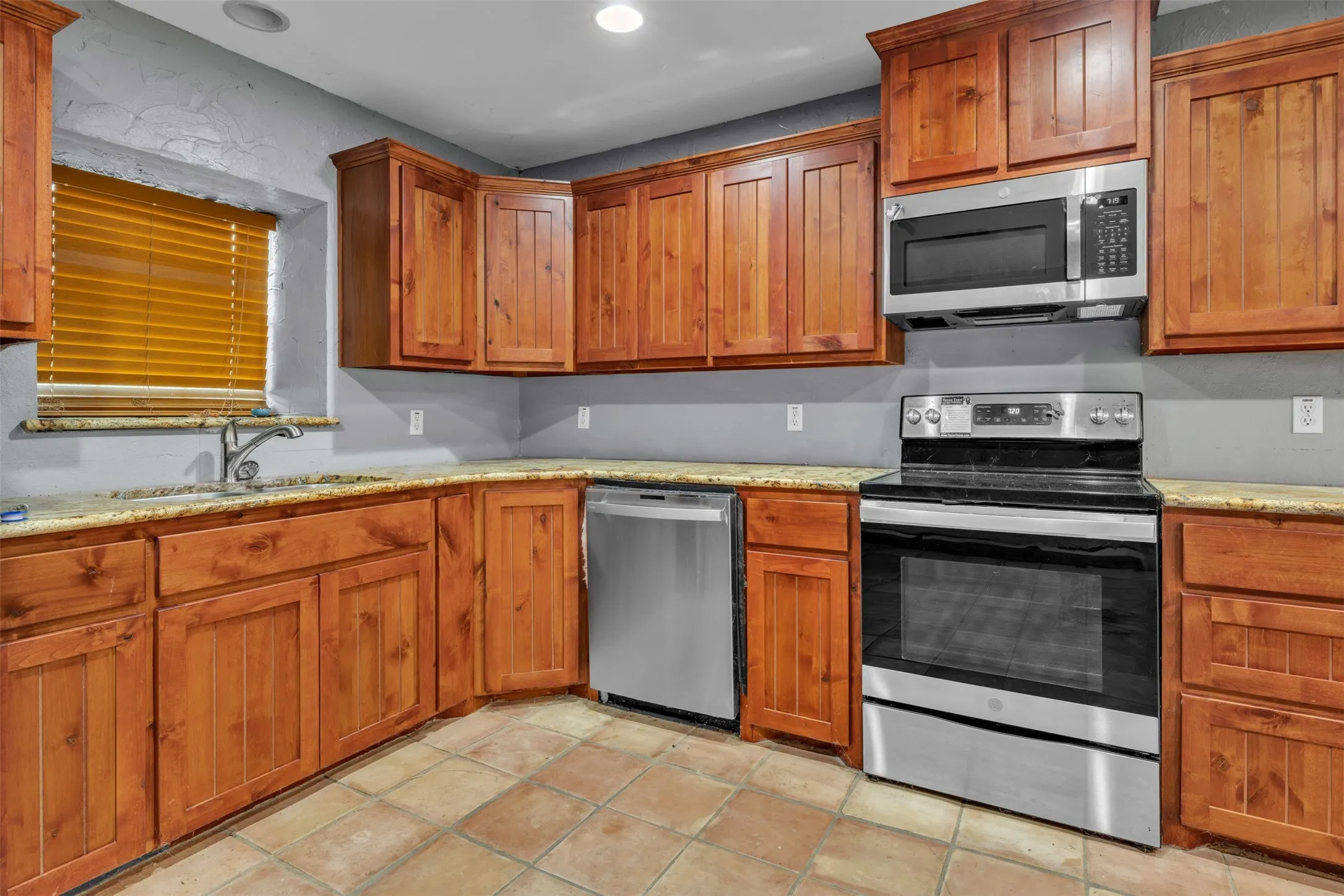 Wood cabinetry with stainless steel appliances, tiled flooring, and light-toned countertops