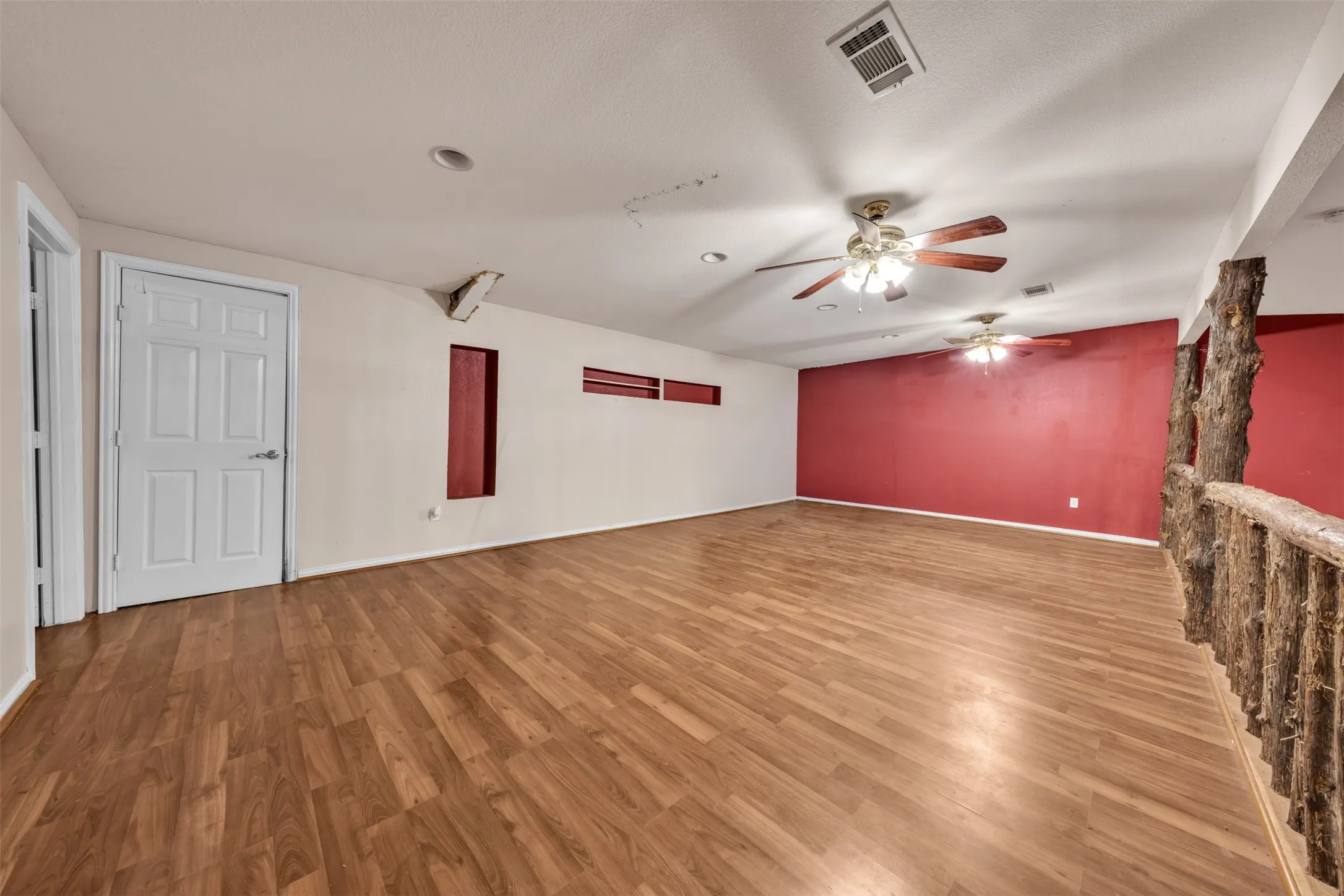 Wood-finish flooring throughout, multiple ceiling fans, recessed lighting, and a decorative wood-textured railing