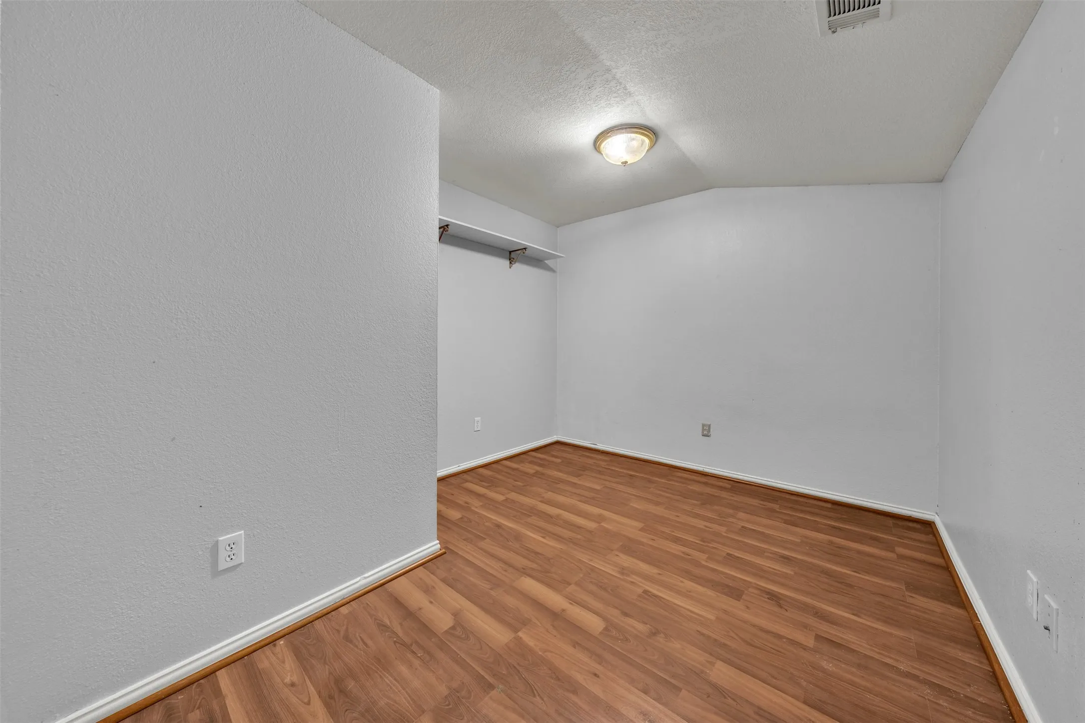 Wood-finish flooring, light gray walls, built-in shelving, and a ceiling-mounted light fixture
