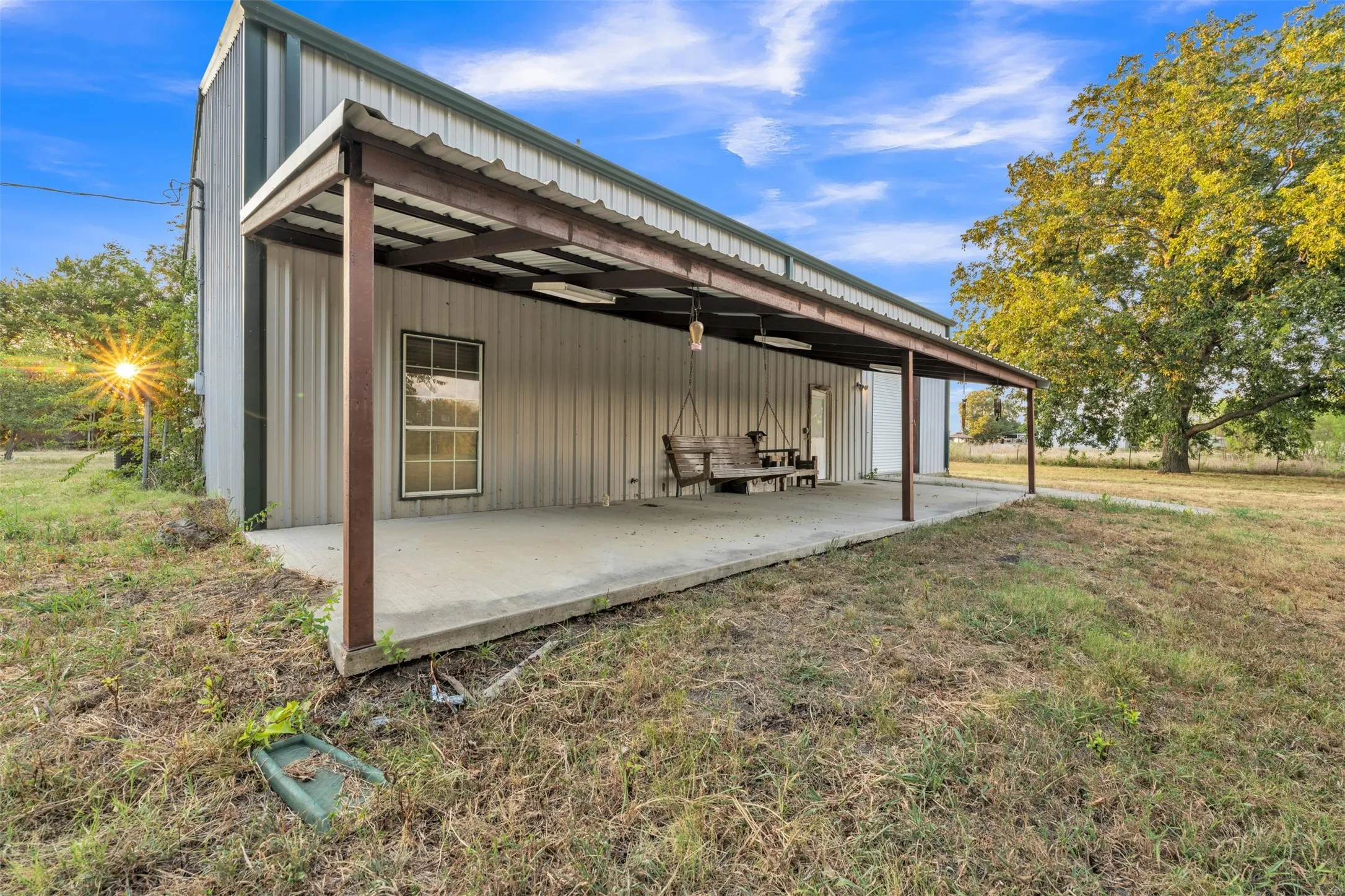 Metal-sided structure featuring a covered concrete patio with a corrugated roof, supported by sturdy posts