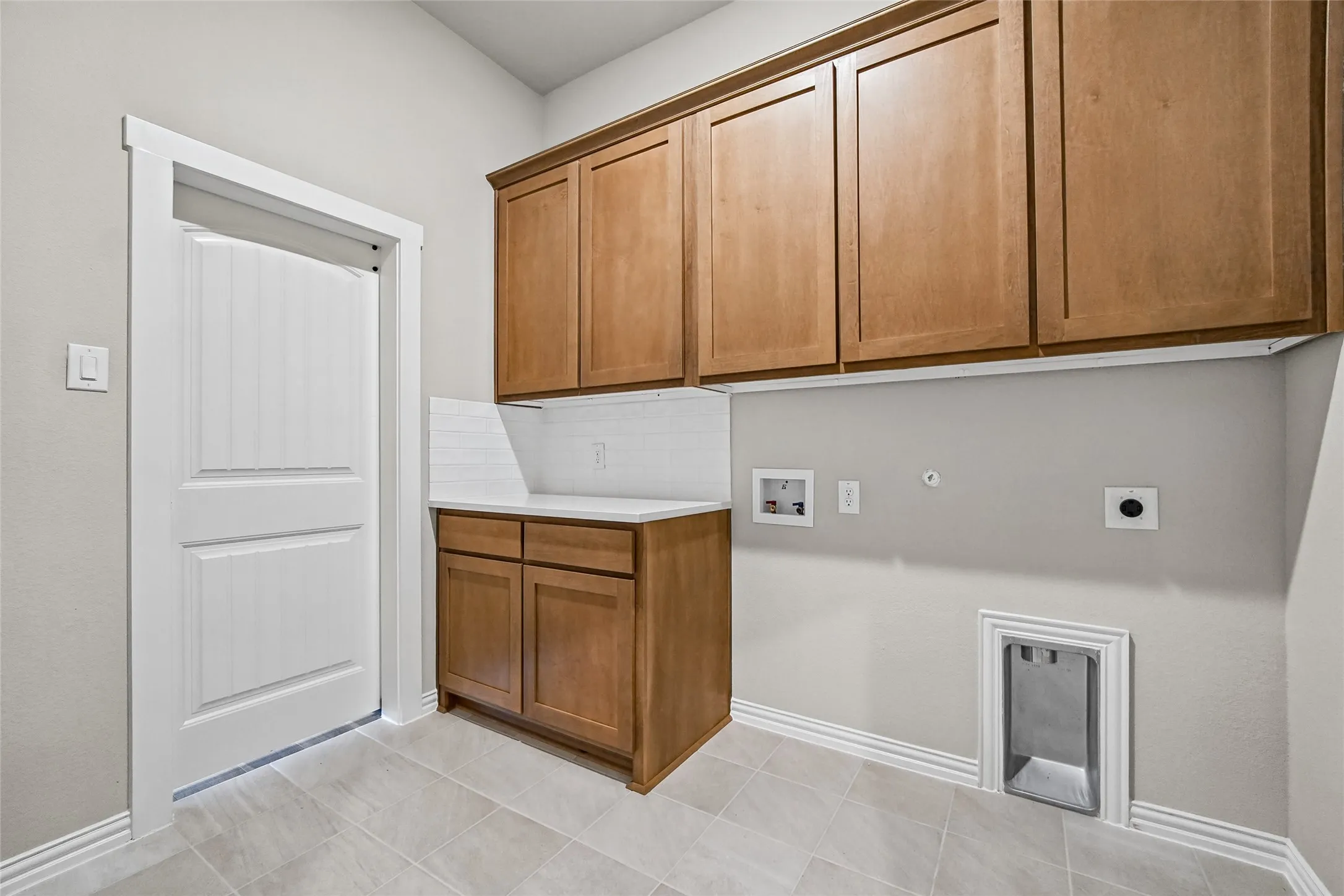Utility room featuring stained wood cabinetry, a white countertop, subway tile backsplash, and ceramic tile flooring