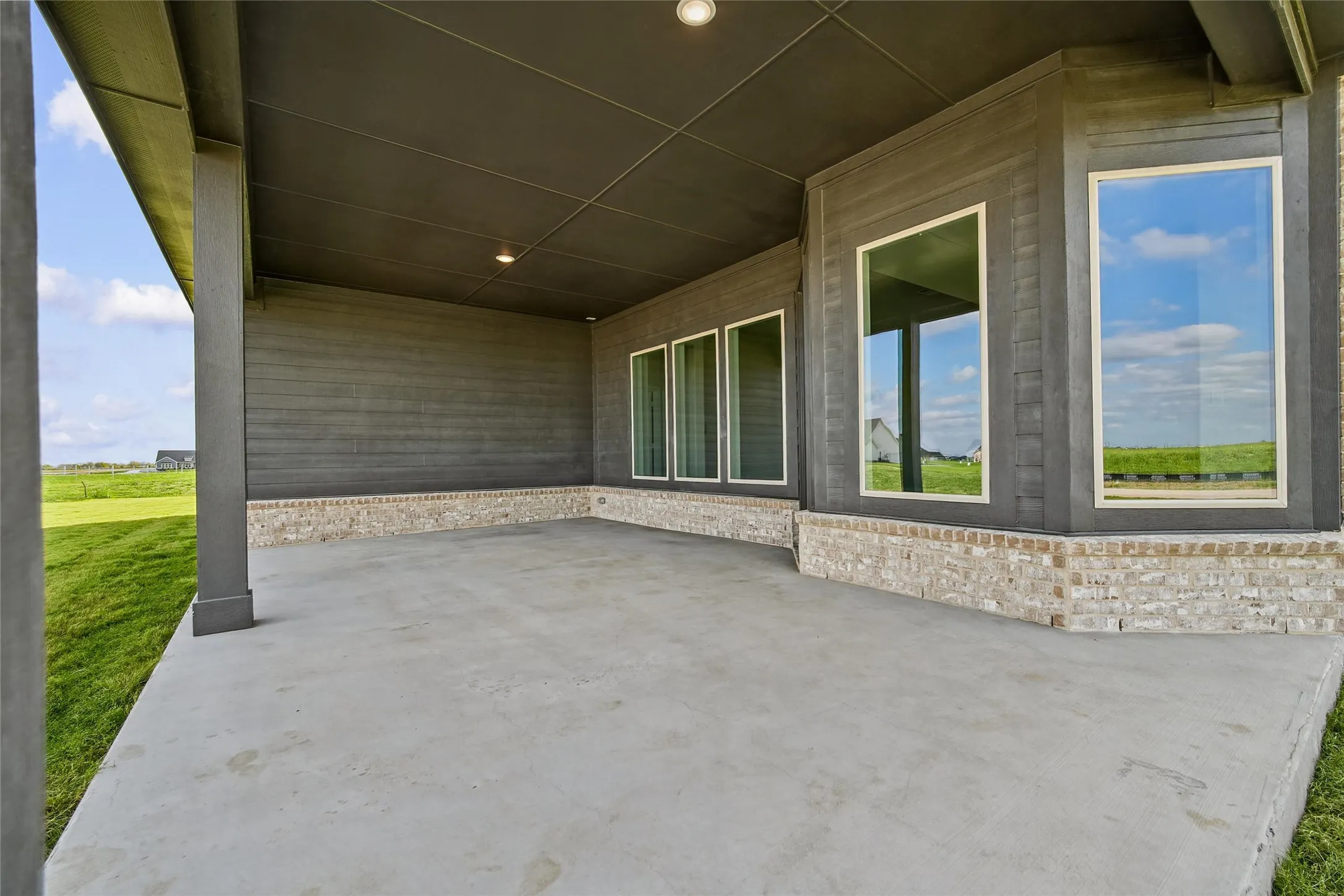 Expansive covered patio featuring a polished concrete floor, stone veneer accents, and multiple glass doors opening to sweeping countryside vistas