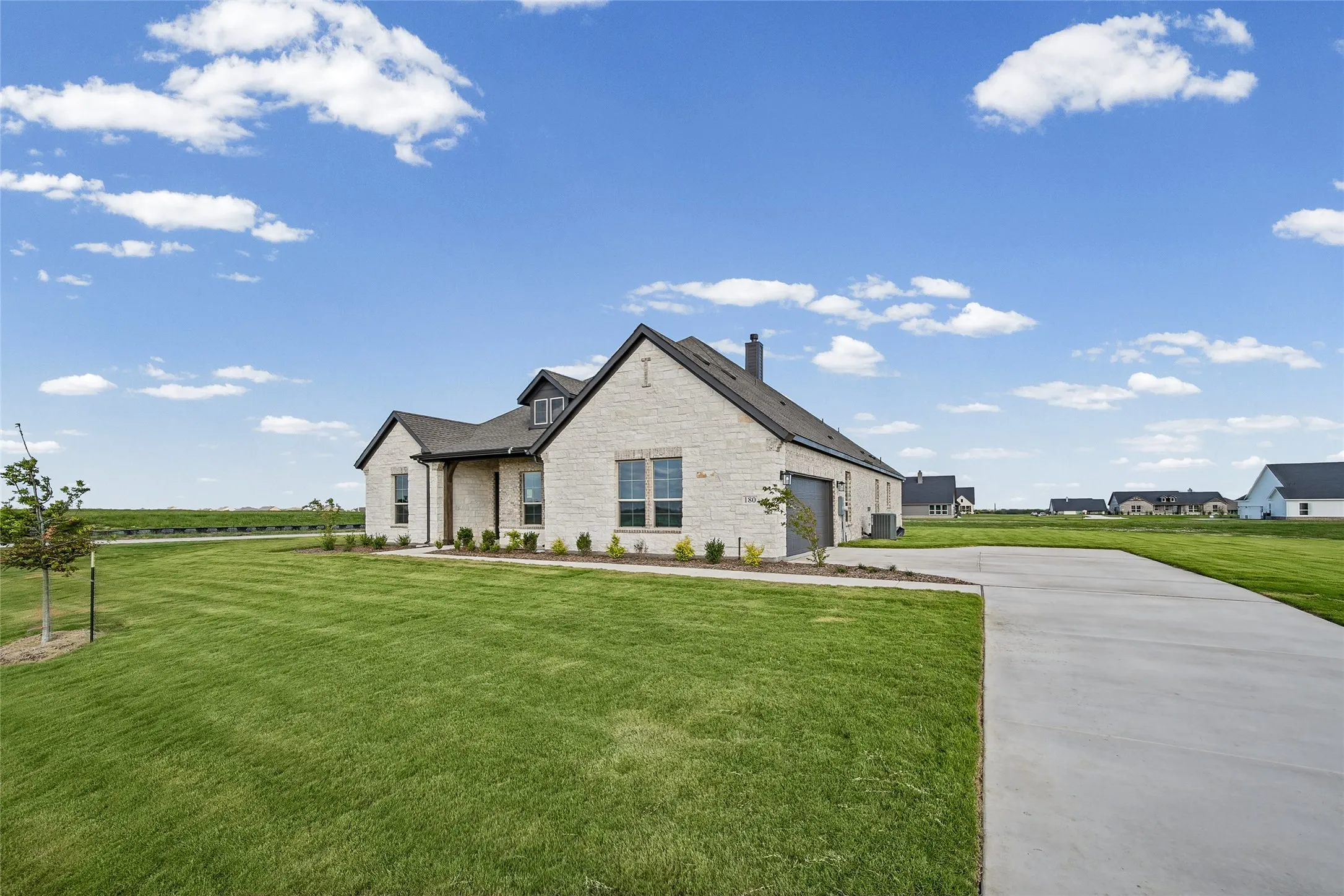 Single-story residence featuring a light-toned stone facade, dark-toned roof shingles, a covered entryway, and an expansive concrete driveway