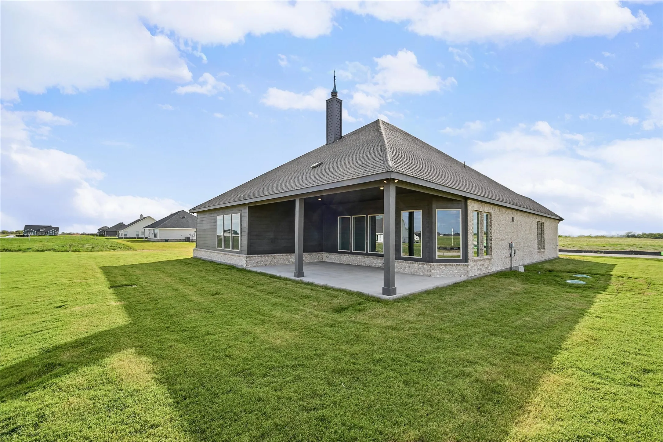 Rear exterior featuring a covered concrete patio, brick and siding facade, hip roof, and expansive lawn