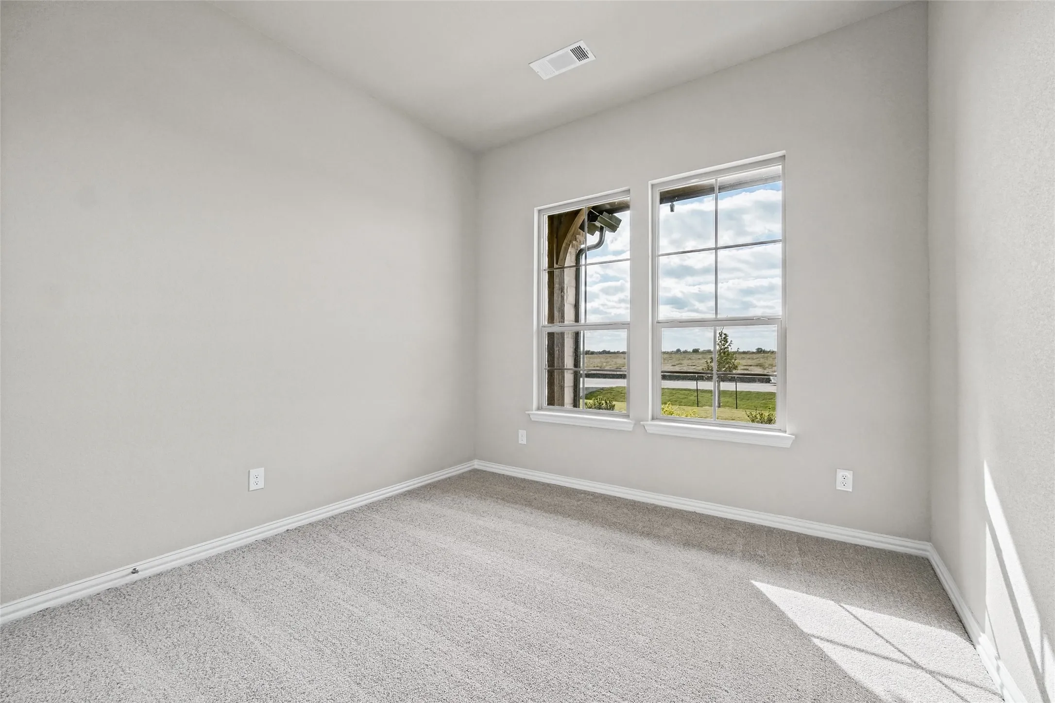 Neutral-toned interior space featuring light-colored wall-to-wall carpeting, dual grid-patterned windows, and monochromatic painted walls