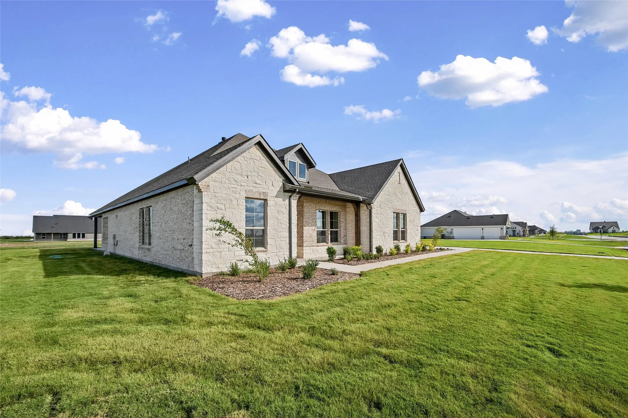 Light-colored masonry exterior featuring a multi-gabled roofline, dual dormer windows, and a manicured lawn