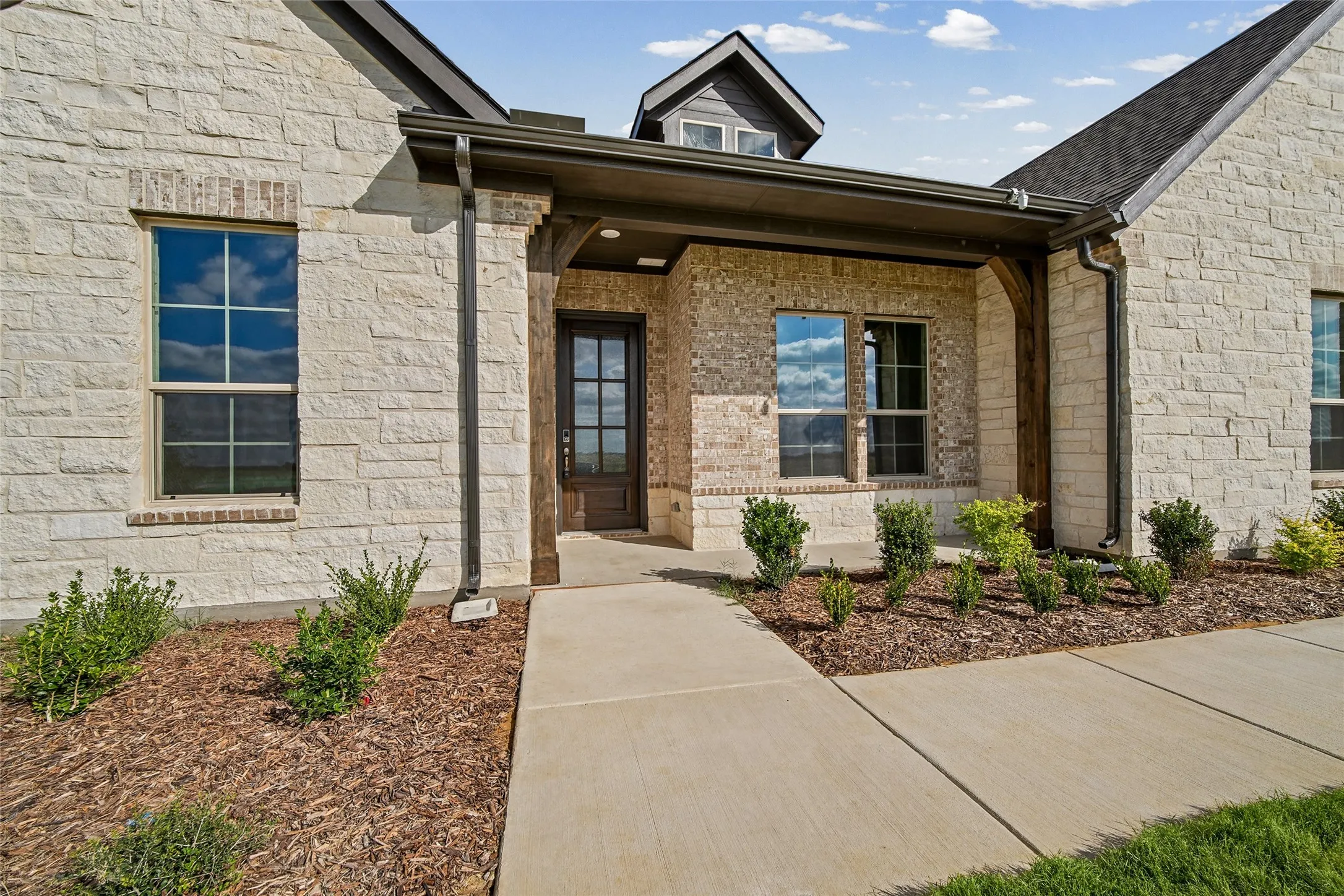 Stone exterior featuring a covered entryway with timber post accents, a multi-pane glass door, and double-hung windows