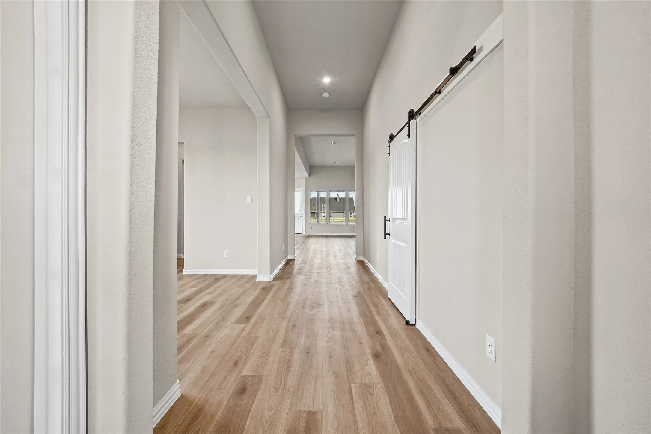 Hallway featuring wood-finish flooring, a white sliding barn door with black iron hardware, and recessed ceiling lighting