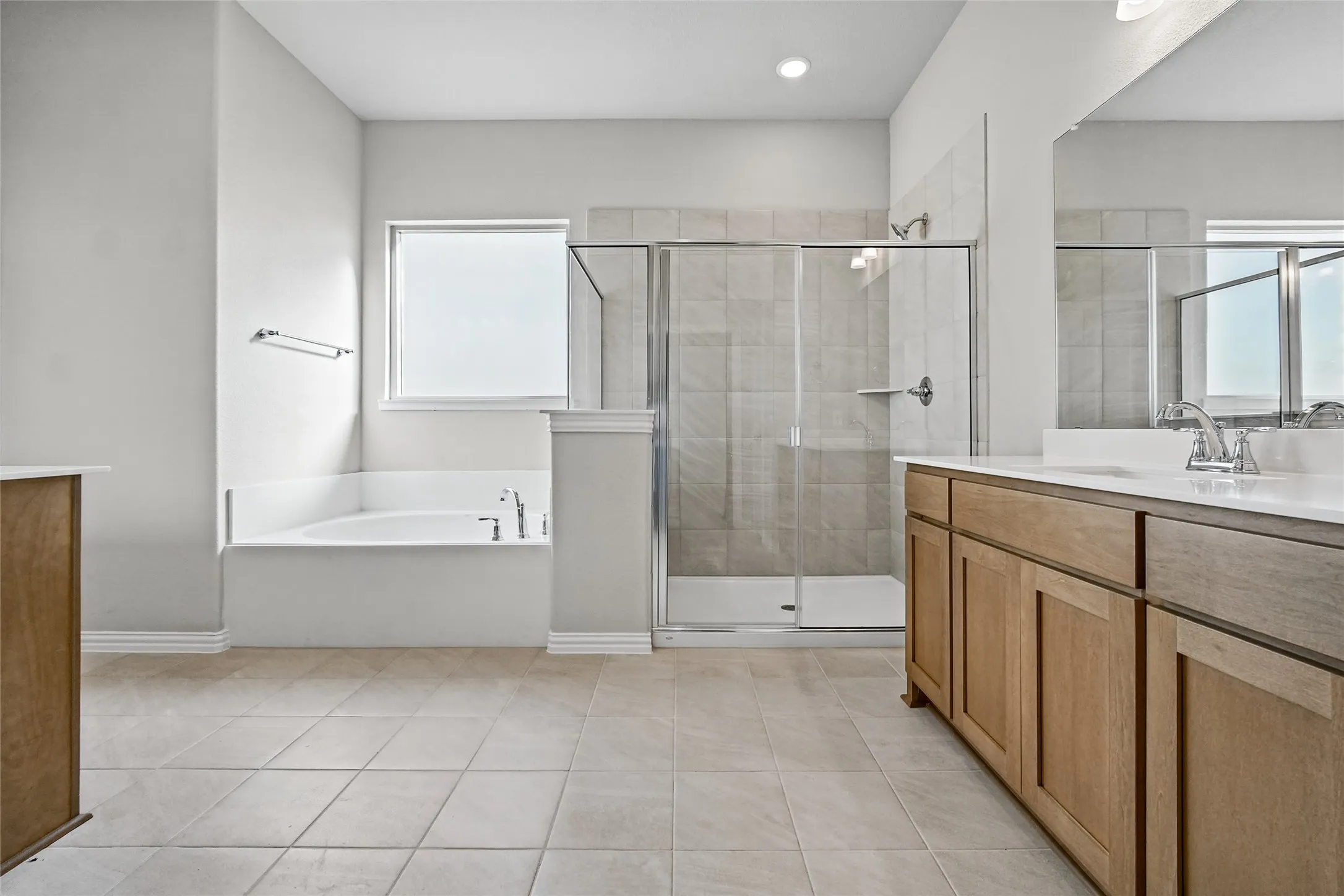 Bathroom featuring a walk-in shower with glass enclosure, soaking tub, light-toned tile flooring, and wood-finish cabinetry with a dual-sink vanity