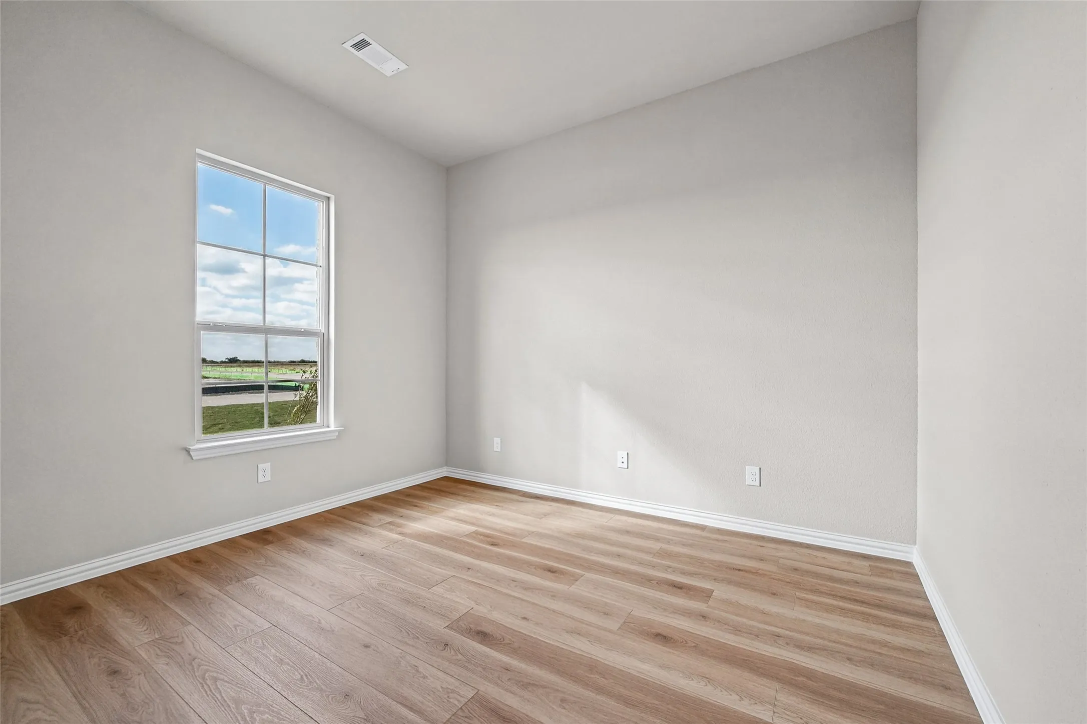 Room featuring light-toned wood-finish flooring, neutral walls, and a single-hung window with a grid pattern