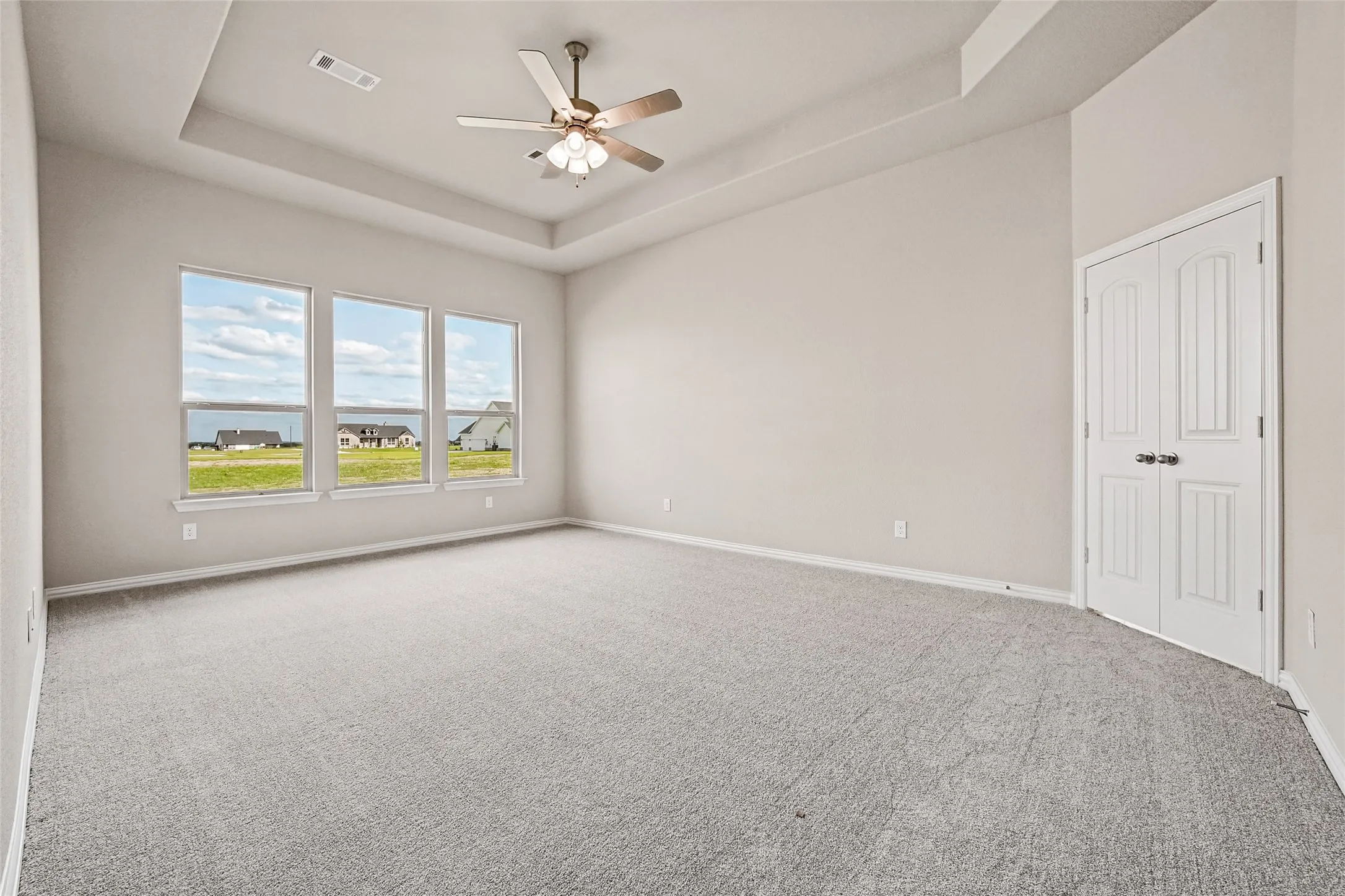 Tray ceiling, neutral wall tones, carpeted flooring, multi-pane windows, and white double-door entry
