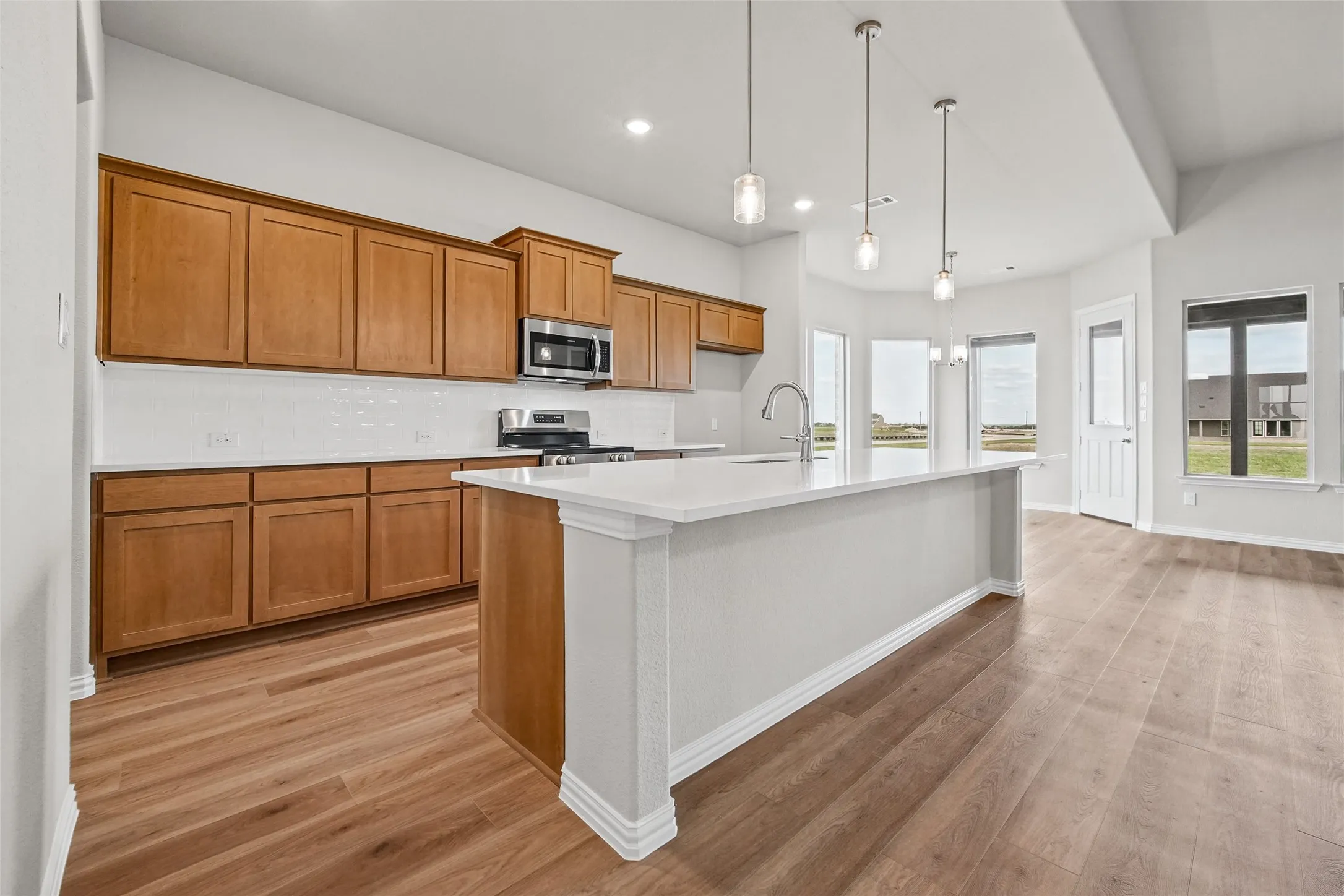 Kitchen featuring wood-finish cabinetry, a large central island with a solid-surface countertop, white tile backsplash, stainless steel appliances, and recessed lighting