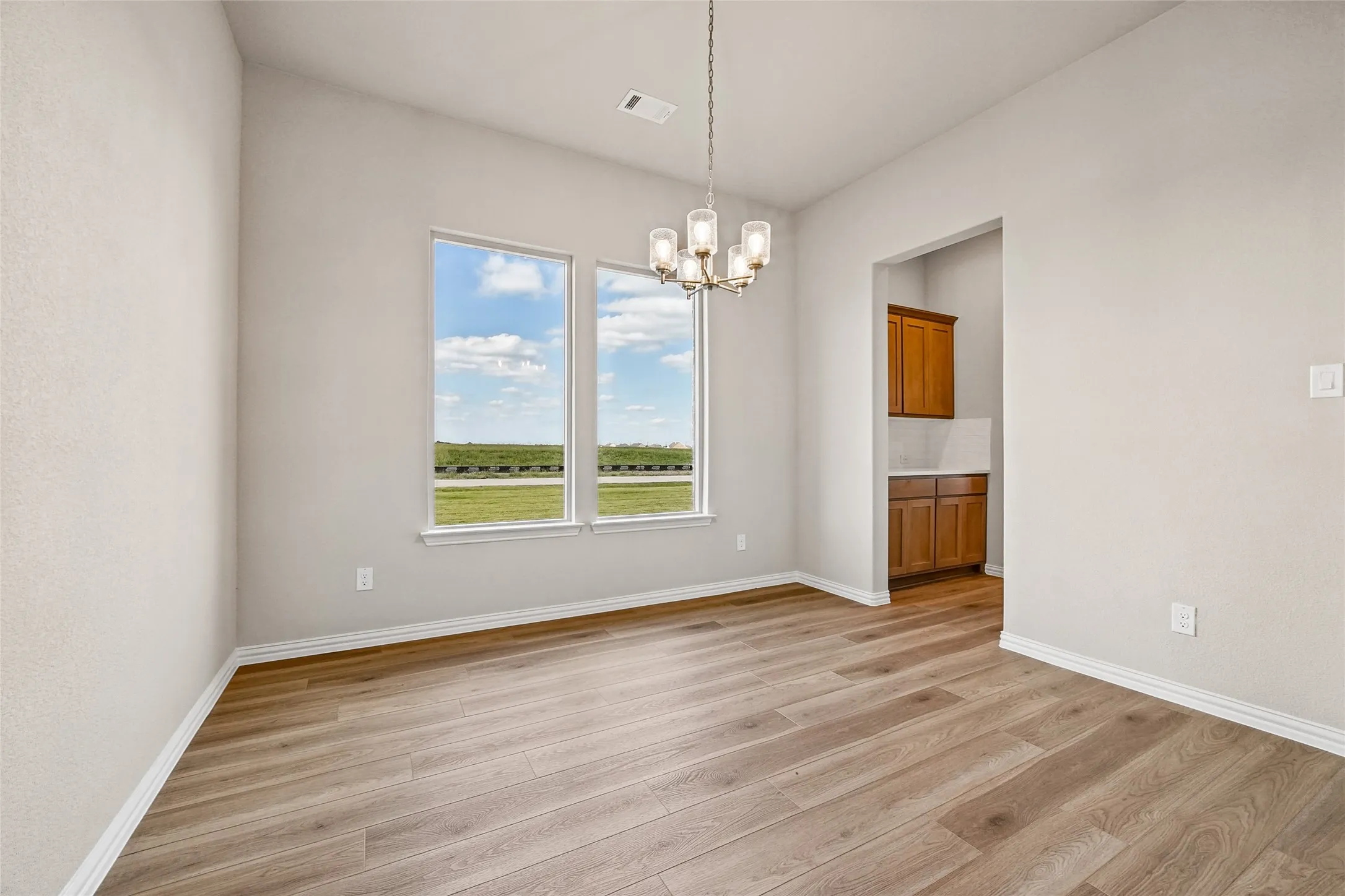 Neutral-toned interior featuring wood-finish flooring, dual windows with exterior scenery, a multi-light chandelier, and built-in wood cabinetry with tile backsplash