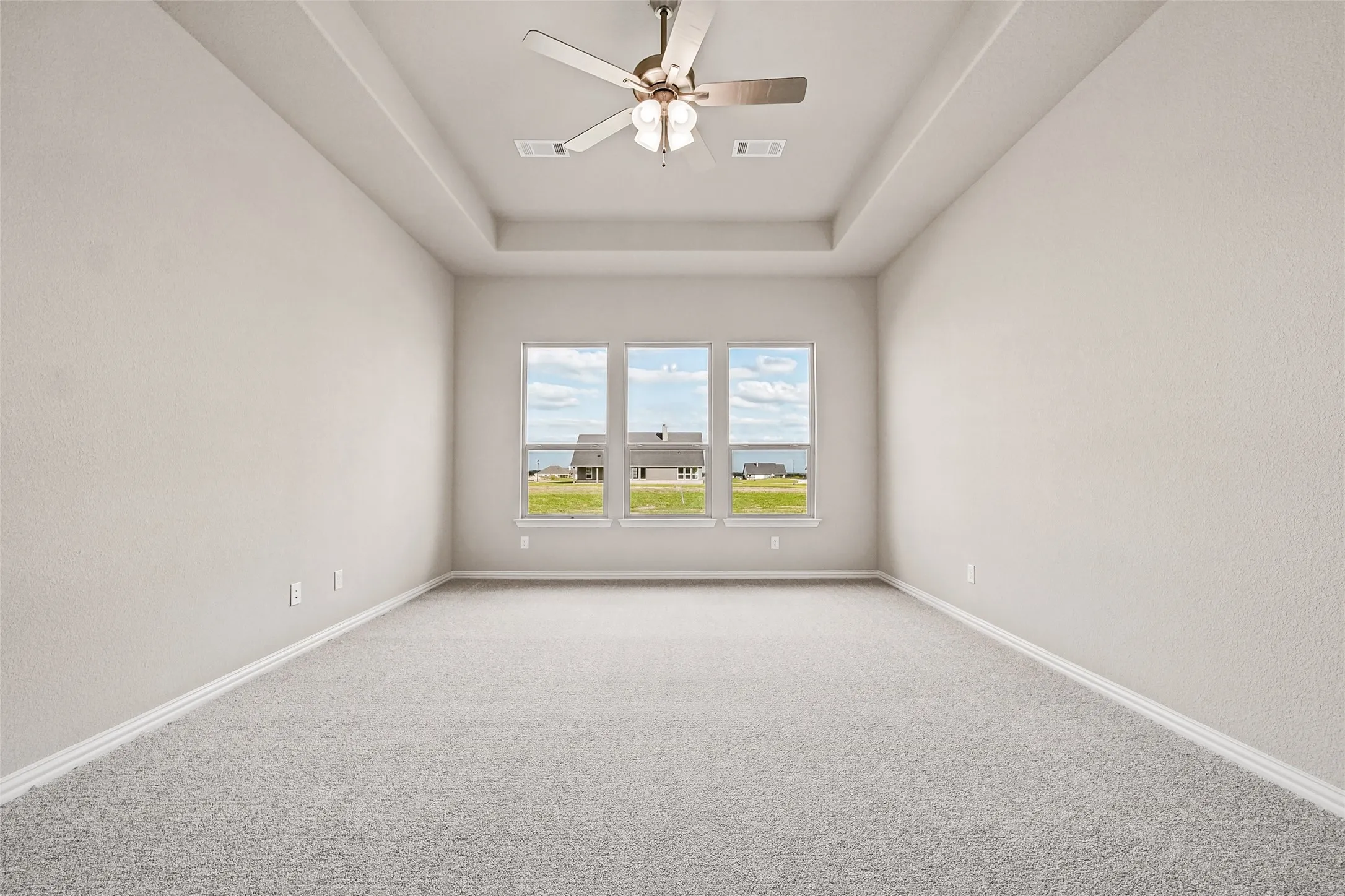 Room featuring a tray ceiling, neutral wall tones, plush wall-to-wall carpeting, a central ceiling fan with integrated lighting, and a trio of energy-efficient windows