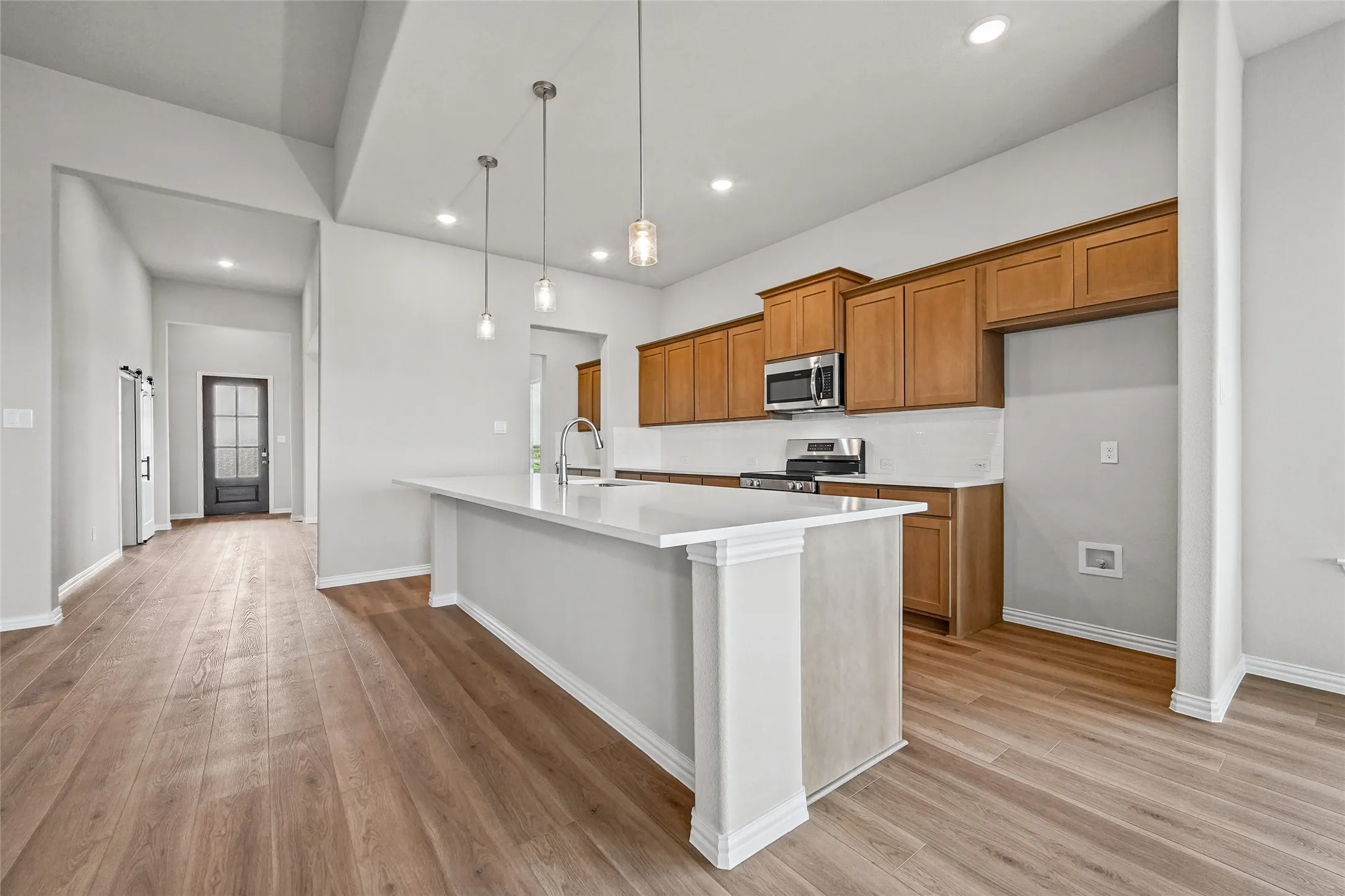 Kitchen featuring wood-finish cabinetry, stone-surface center island with a stainless steel faucet, recessed lighting, pendant lights, and wood-finish flooring