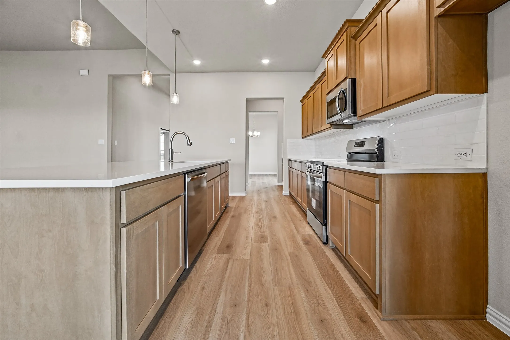 Kitchen featuring wood-finish cabinetry, white solid-surface countertops, subway tile backsplash, stainless steel appliances, and pendant lighting