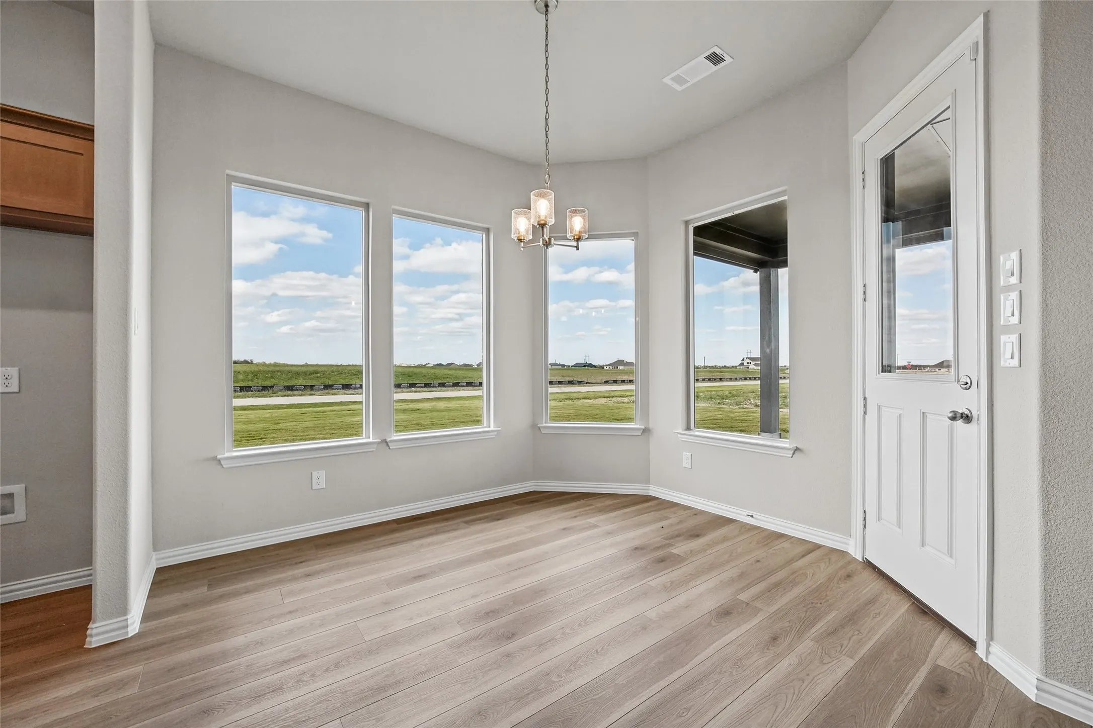 Multi-paneled windows in a bay configuration, wood-finish flooring, brushed nickel multi-light pendant fixture, and glass-paneled exterior door