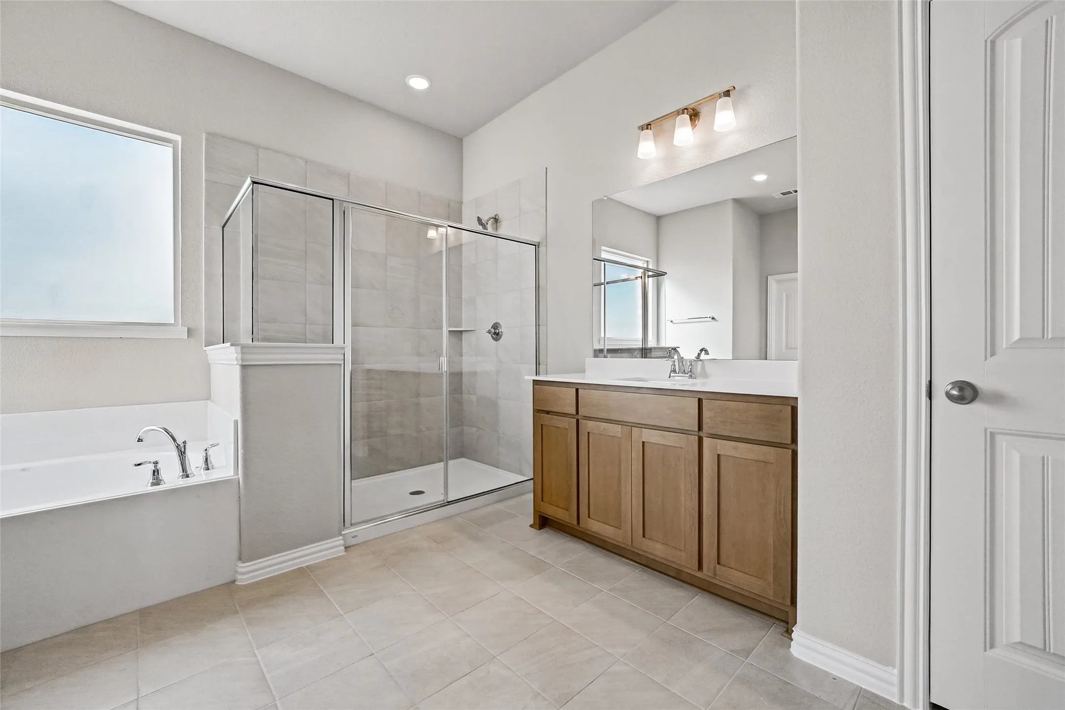 Bathroom featuring a wood-finish vanity with a stone countertop, a separate soaking tub, and a glass-enclosed shower with tile surround