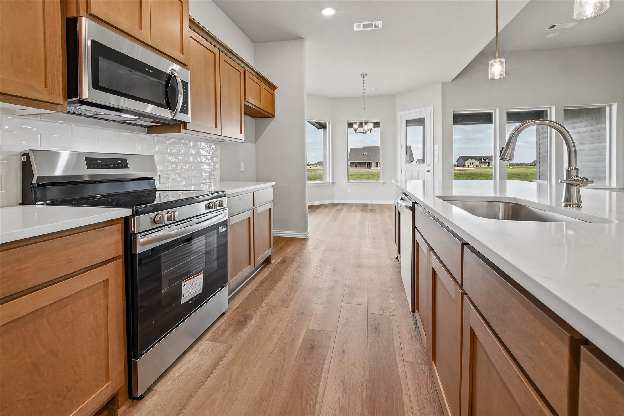 Kitchen featuring wood-finish cabinetry, white solid-surface countertops, subway tile backsplash, stainless steel appliances, and wood-finish flooring