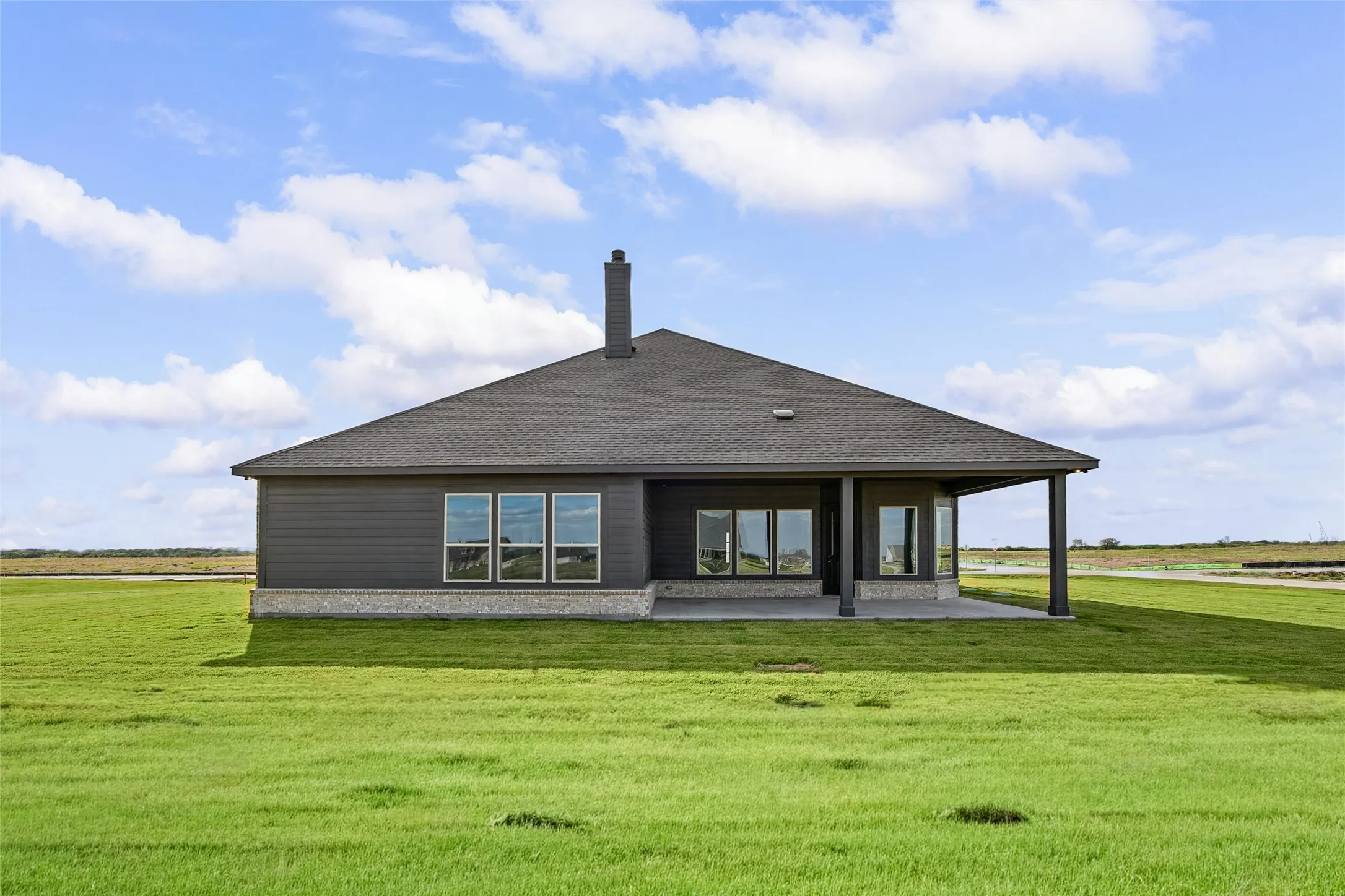 Single-story residence featuring horizontal lap siding, stone veneer base, a covered rear patio, asphalt shingle roof, and a central chimney