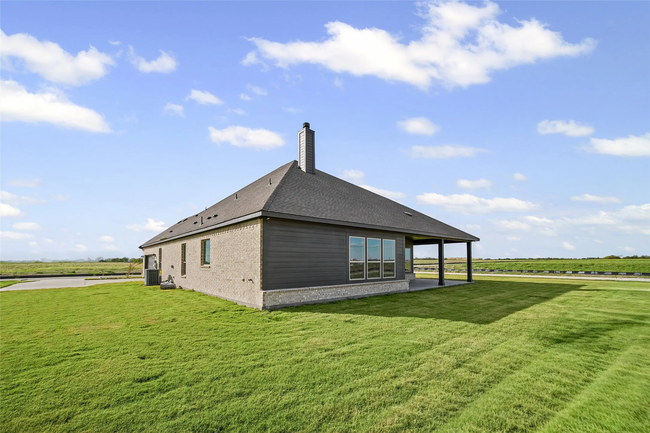 Exterior featuring a combination of brick and horizontal siding, a hipped roof with a chimney, a covered rear patio, and expansive acreage