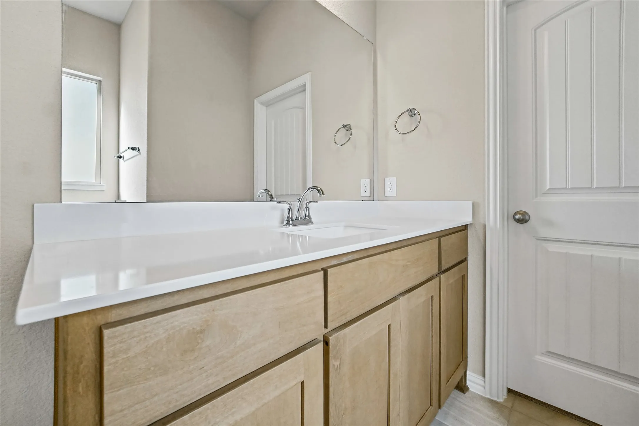 Vanity featuring natural wood-finish cabinetry, white solid-surface countertop with an integrated rectangular sink, polished chrome faucet, and expansive wall-mounted mirror