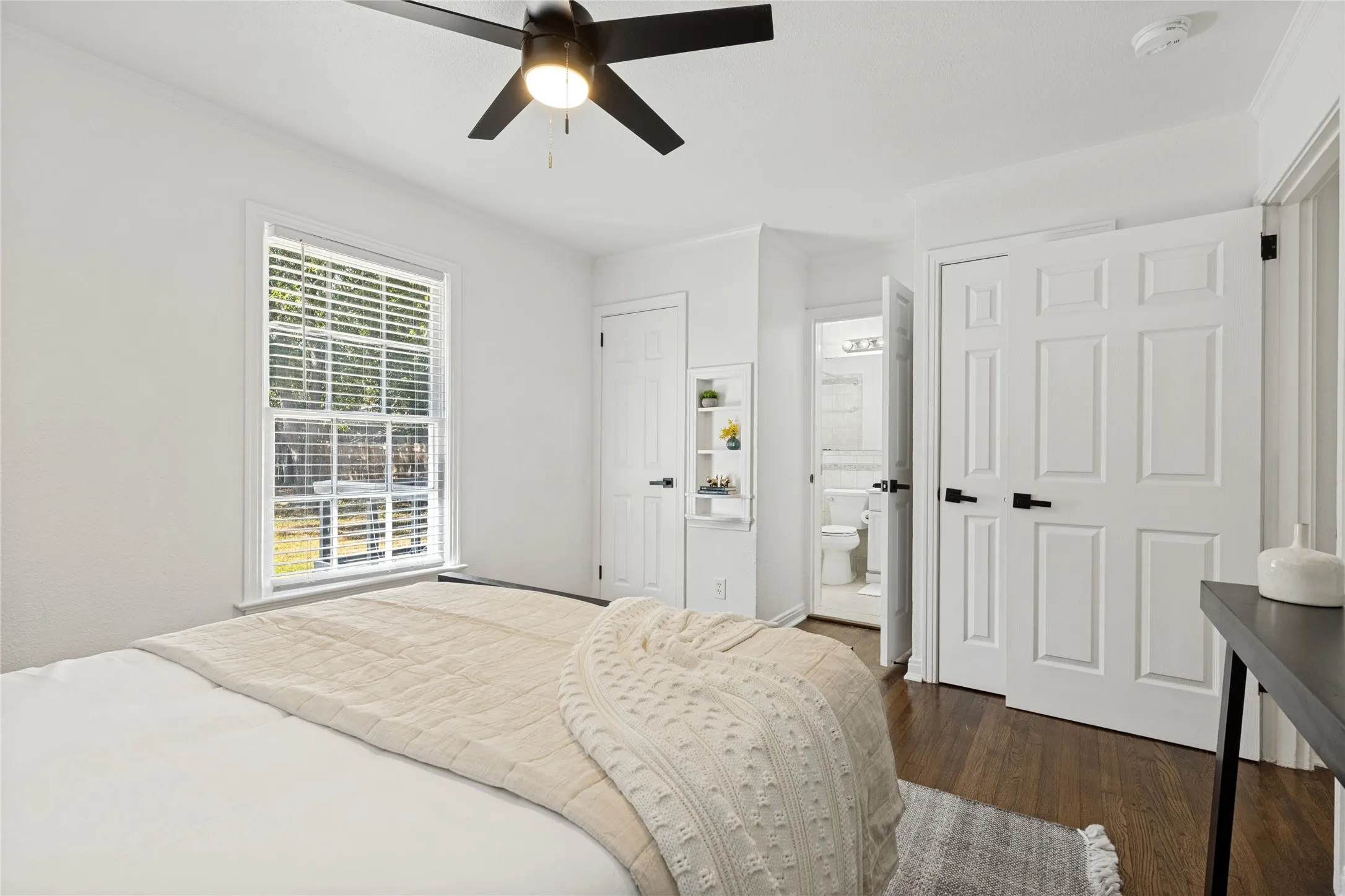 Hardwood-style flooring, a ceiling fan with integrated lighting, a built-in shelving unit, and white paneled doors with dark hardware