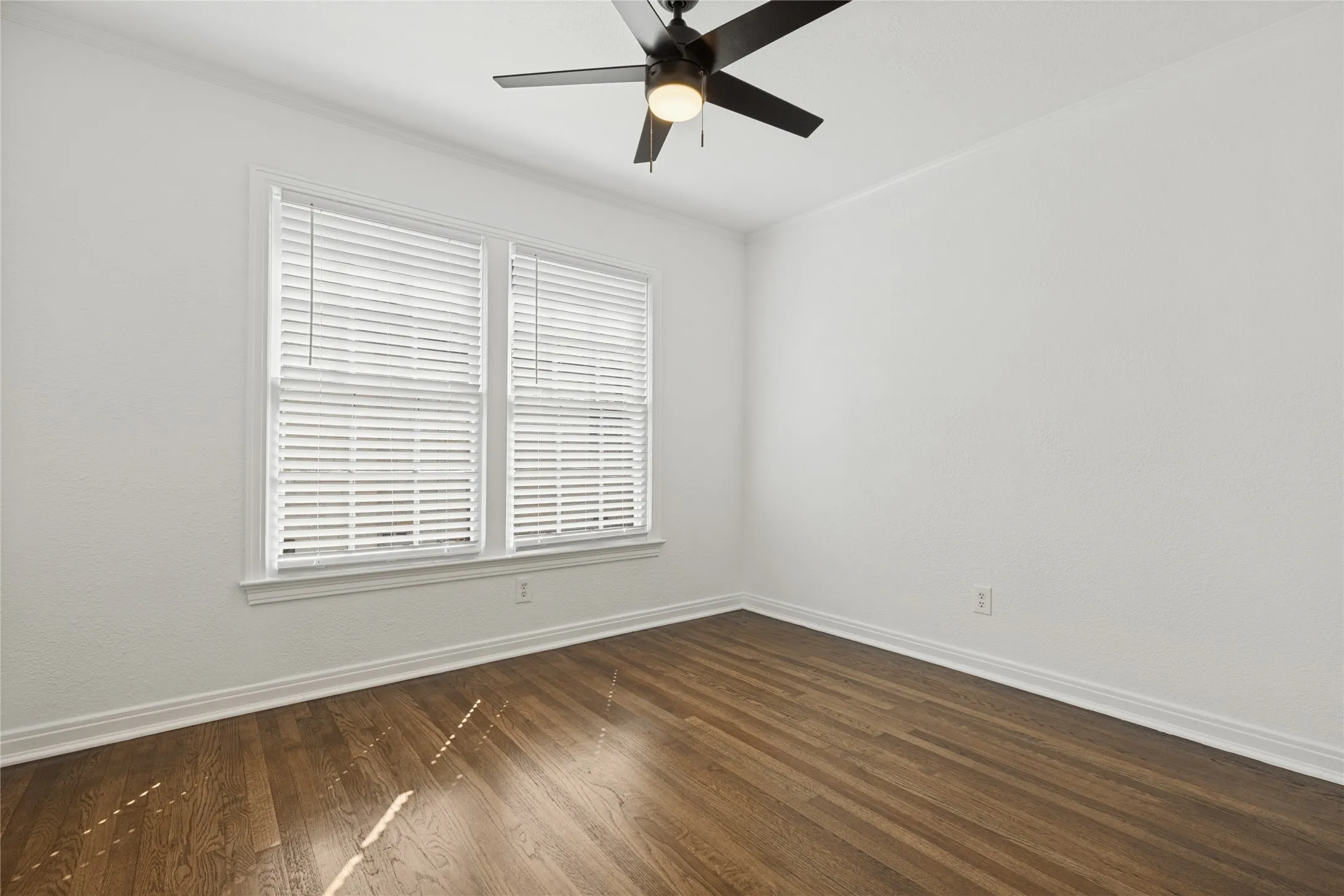 Wood-finish flooring, two windows with blinds, ceiling fan, and white walls