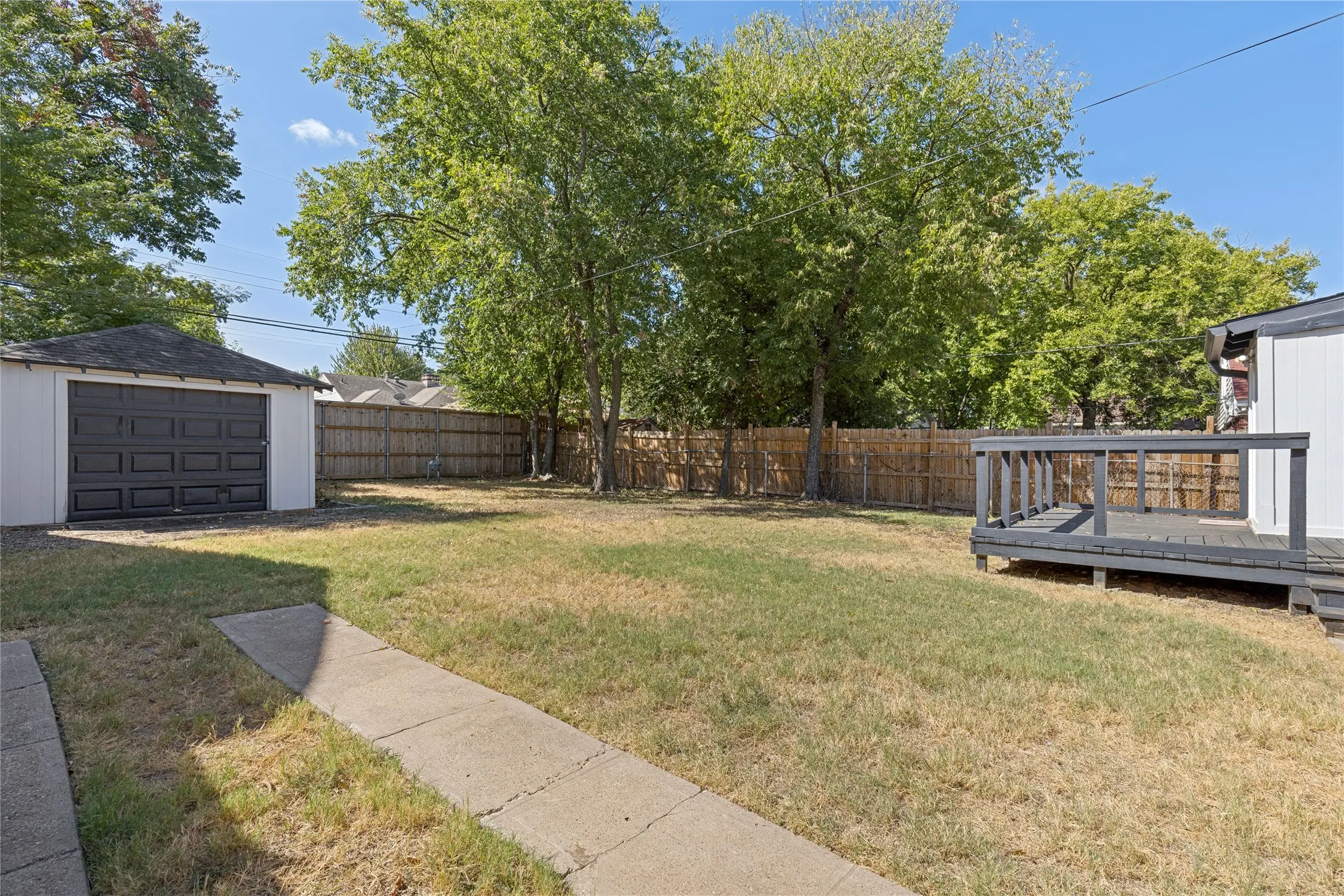 Expansive backyard featuring a concrete walkway, wood privacy fencing, a separate garage structure, and a raised wood deck