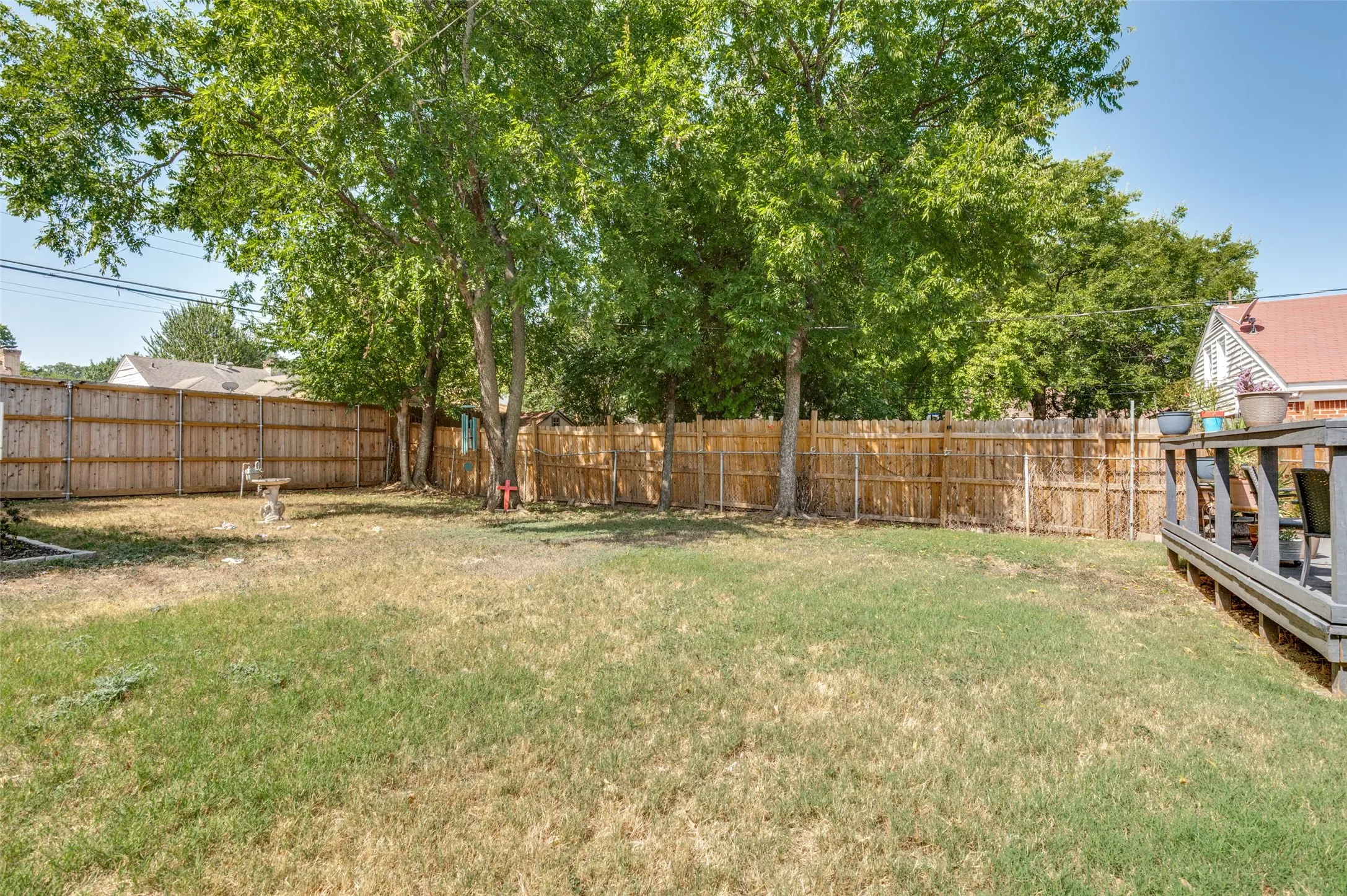 Fenced backyard featuring mature trees and a wood deck