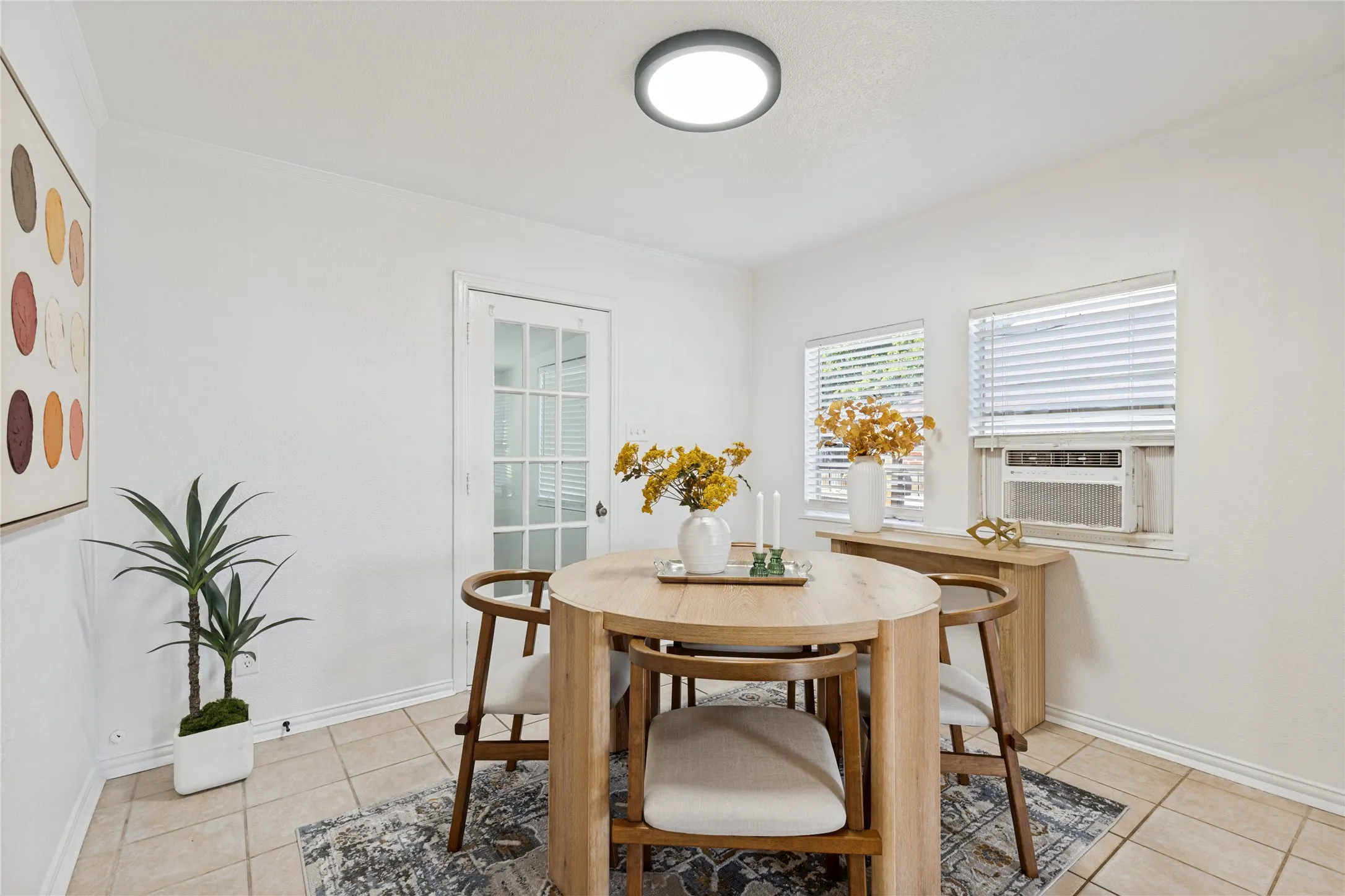 Recessed ceiling light fixture, white walls, two windows with blinds, air conditioning unit, and a French pane door