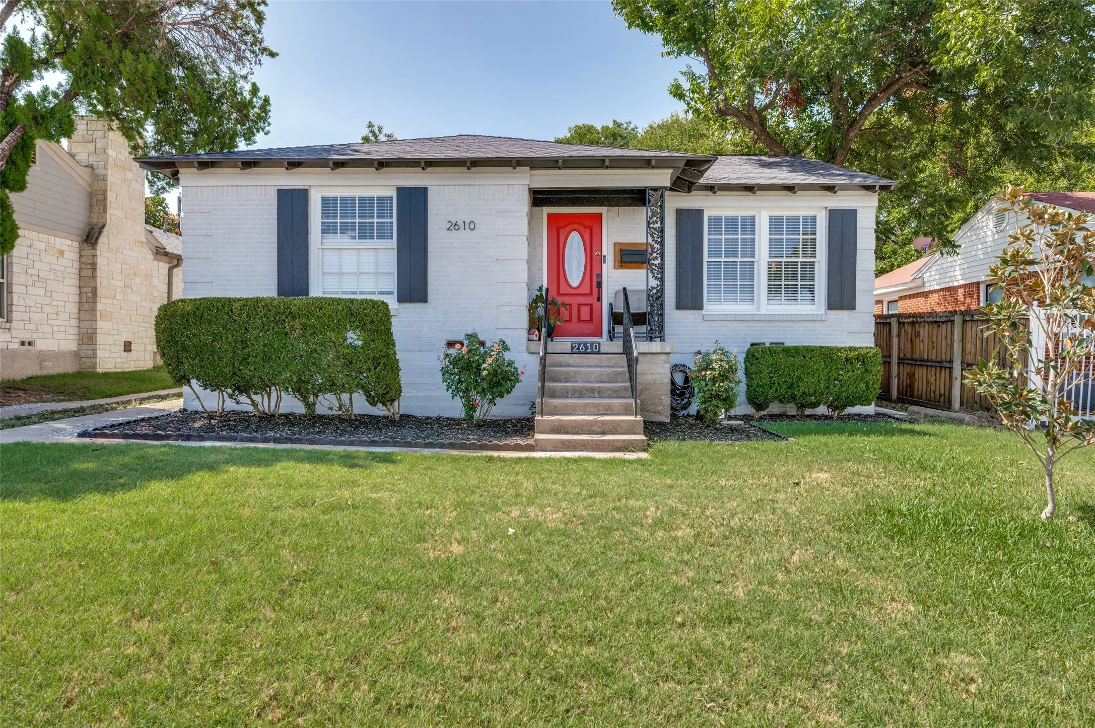 Brick exterior with a vibrant red front door, white-framed windows, and dark shutters