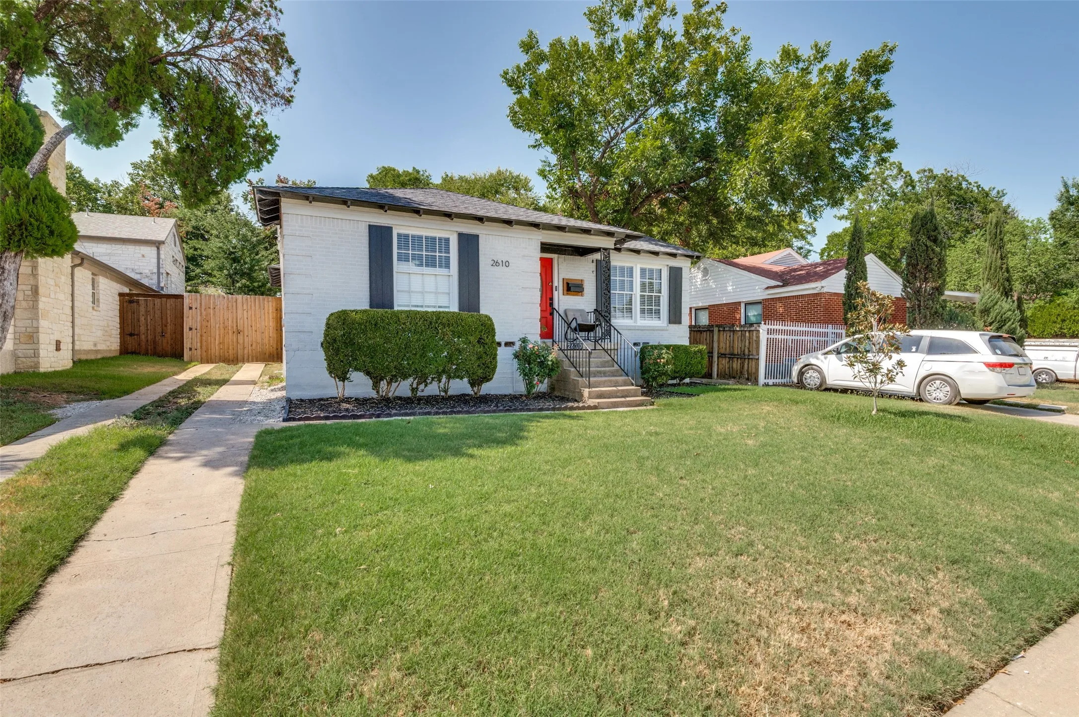 White brick exterior with black shutters, front entry steps, mature landscaping, and a driveway