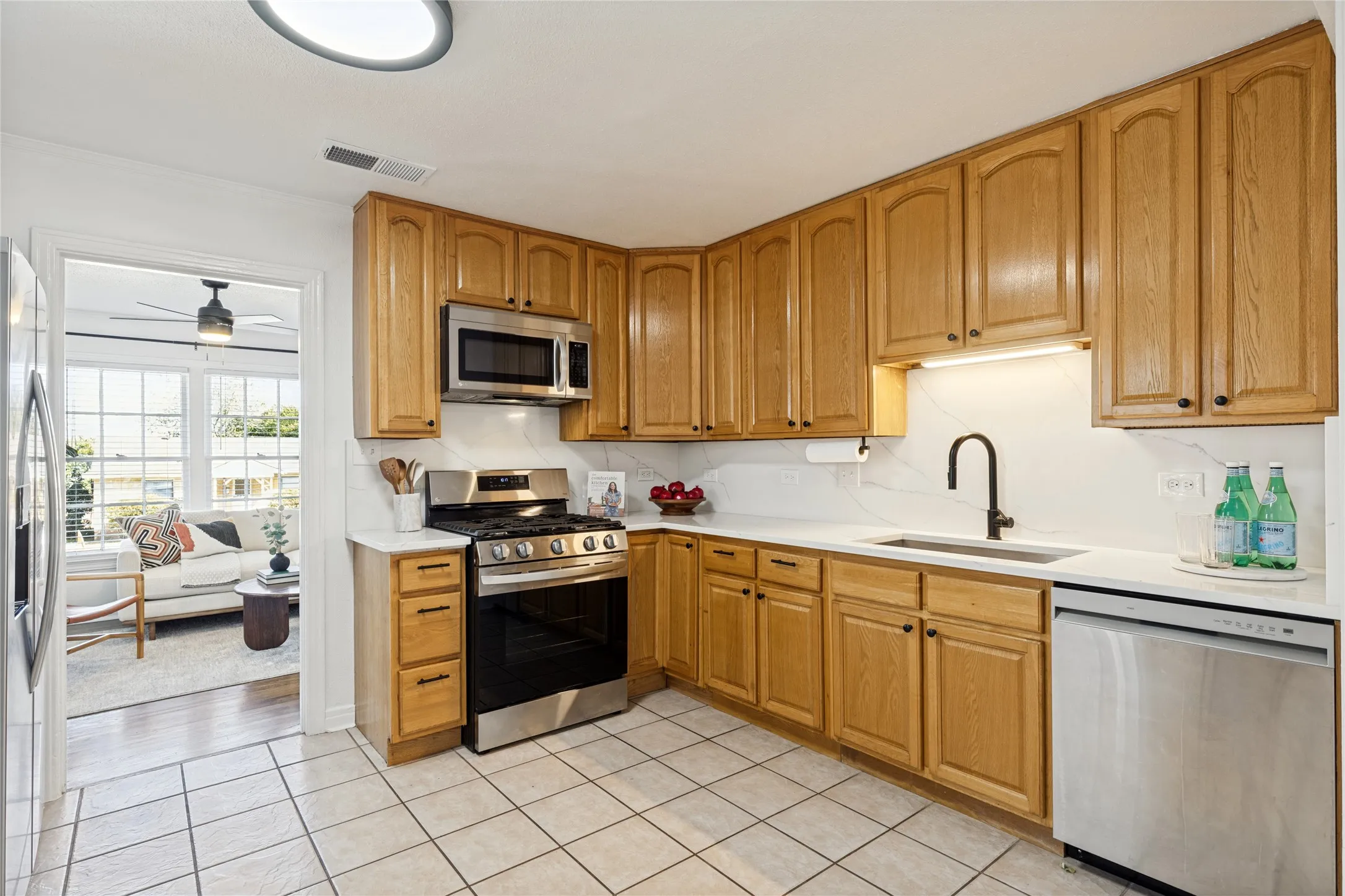 Kitchen featuring wood cabinetry, stainless steel appliances, white countertops, a tiled backsplash, and tiled flooring