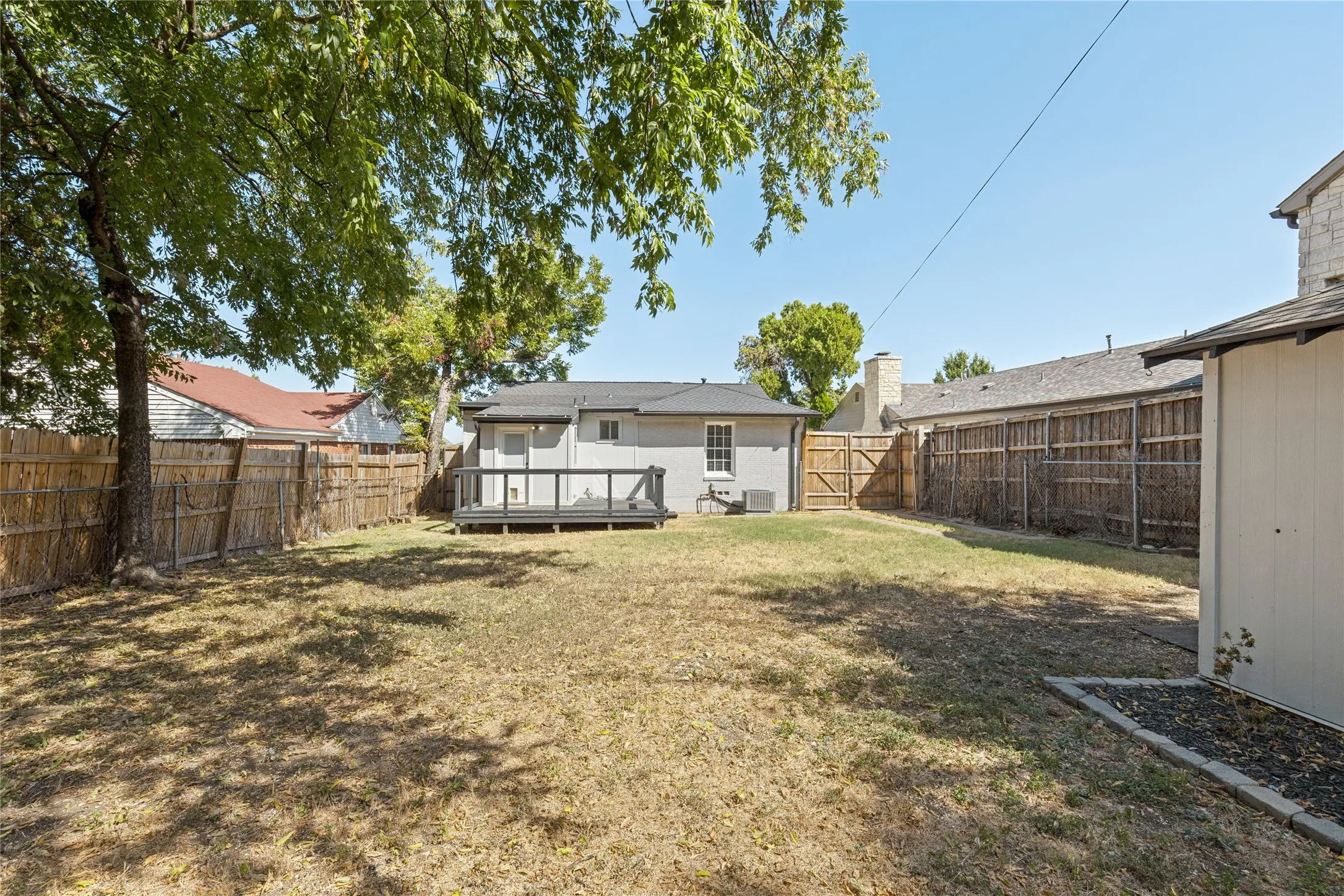 Expansive backyard with a wooden fence, mature tree, and a built-in outdoor deck