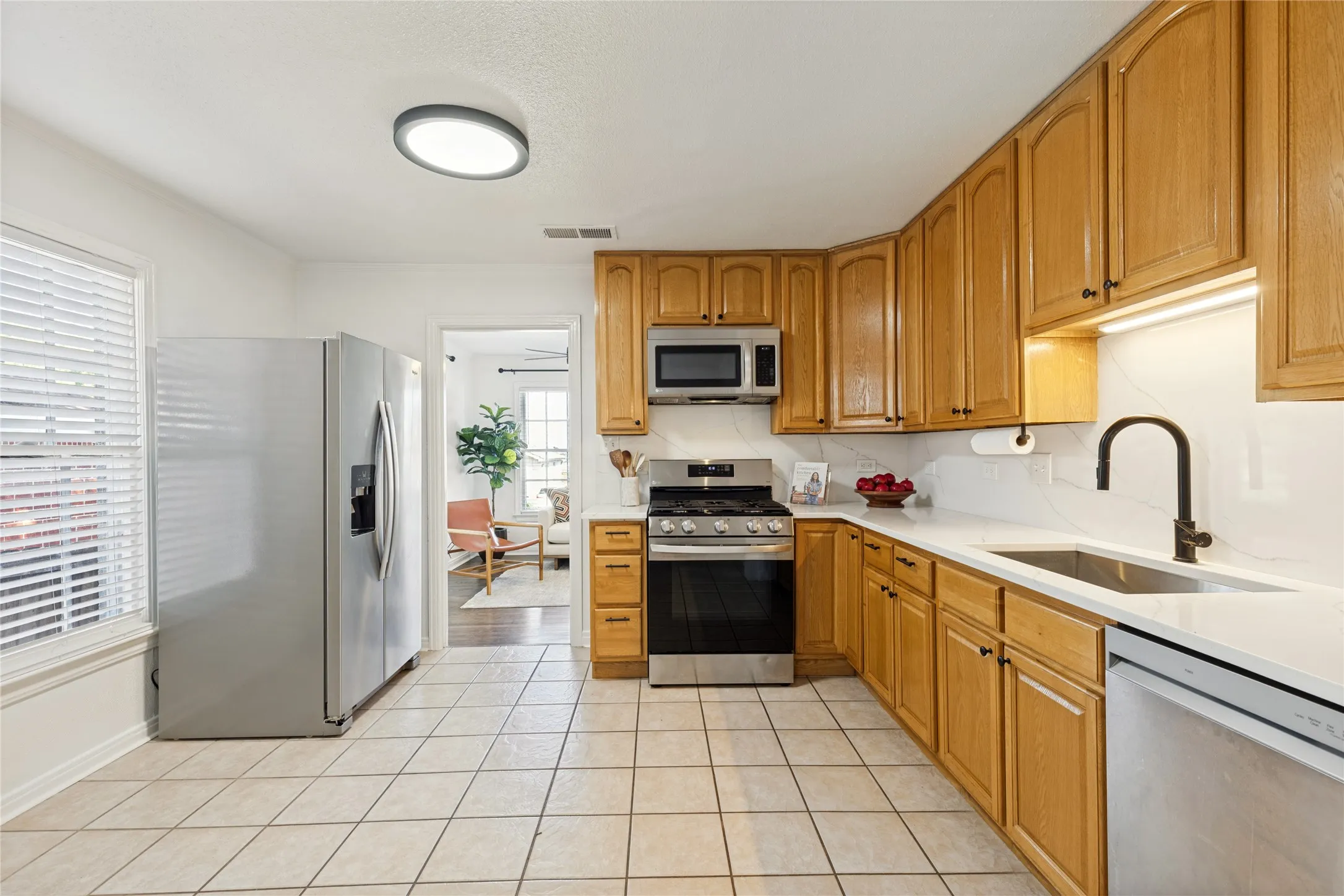 Kitchen featuring wood cabinetry, stainless steel appliances, tile flooring, and quartz countertops with a white subway tile backsplash