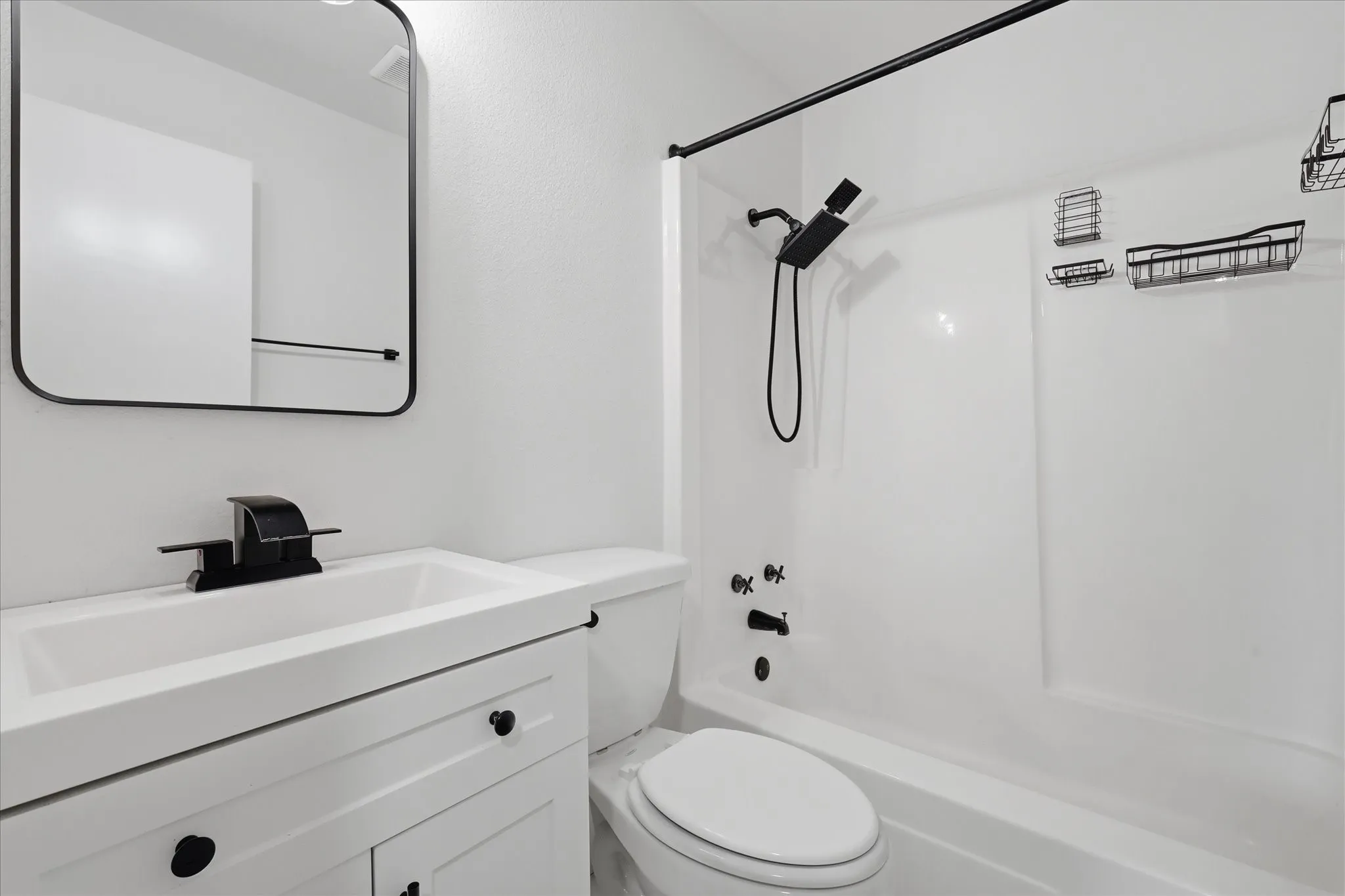 Full bathroom featuring a white vanity with integrated sink, black hardware, a shower-tub combination, and a contemporary mirror