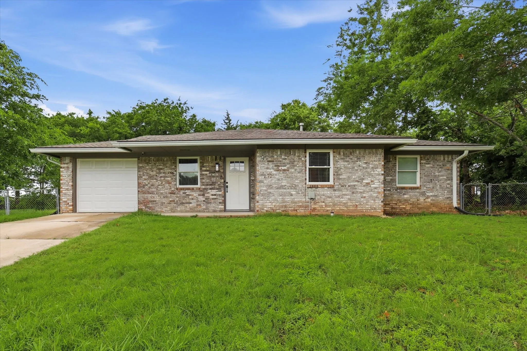 Brick facade with a single-car garage, mature trees, and a concrete driveway